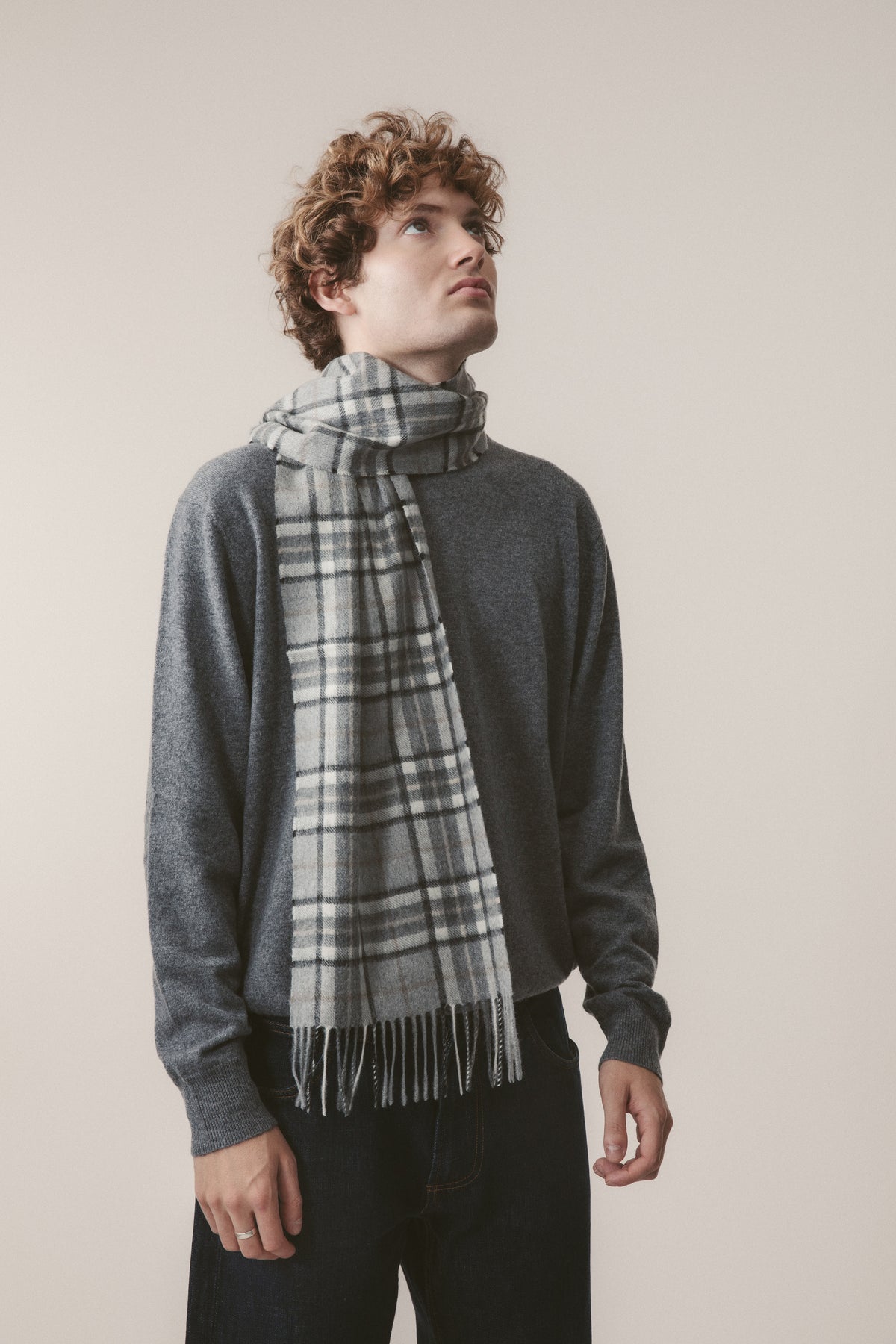 Scotty Thompson Cashmere Scarf in Pewter, grey plaid pattern with fringed ends, styled loosely around the neck over a charcoal sweater