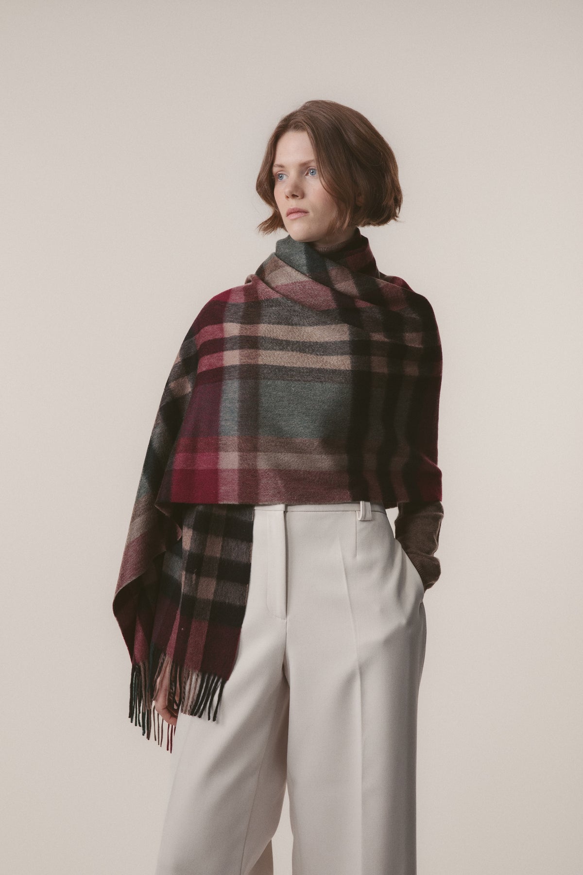 Model wearing Tartan 2 Cashmere Stole in Burgundy Rust draped over shoulders, showing plaid pattern with fringe detail