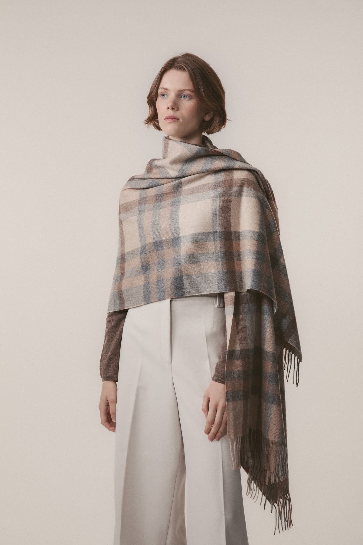 Tartan 2 Cashmere Stole in Natural draped over shoulders, featuring soft plaid pattern in beige, blue, and brown with fringed edges