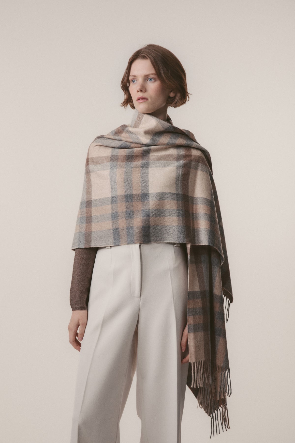 Model wearing the Tartan 2 Cashmere Stole in Natural draped over shoulders, showing the soft plaid pattern with fringed ends