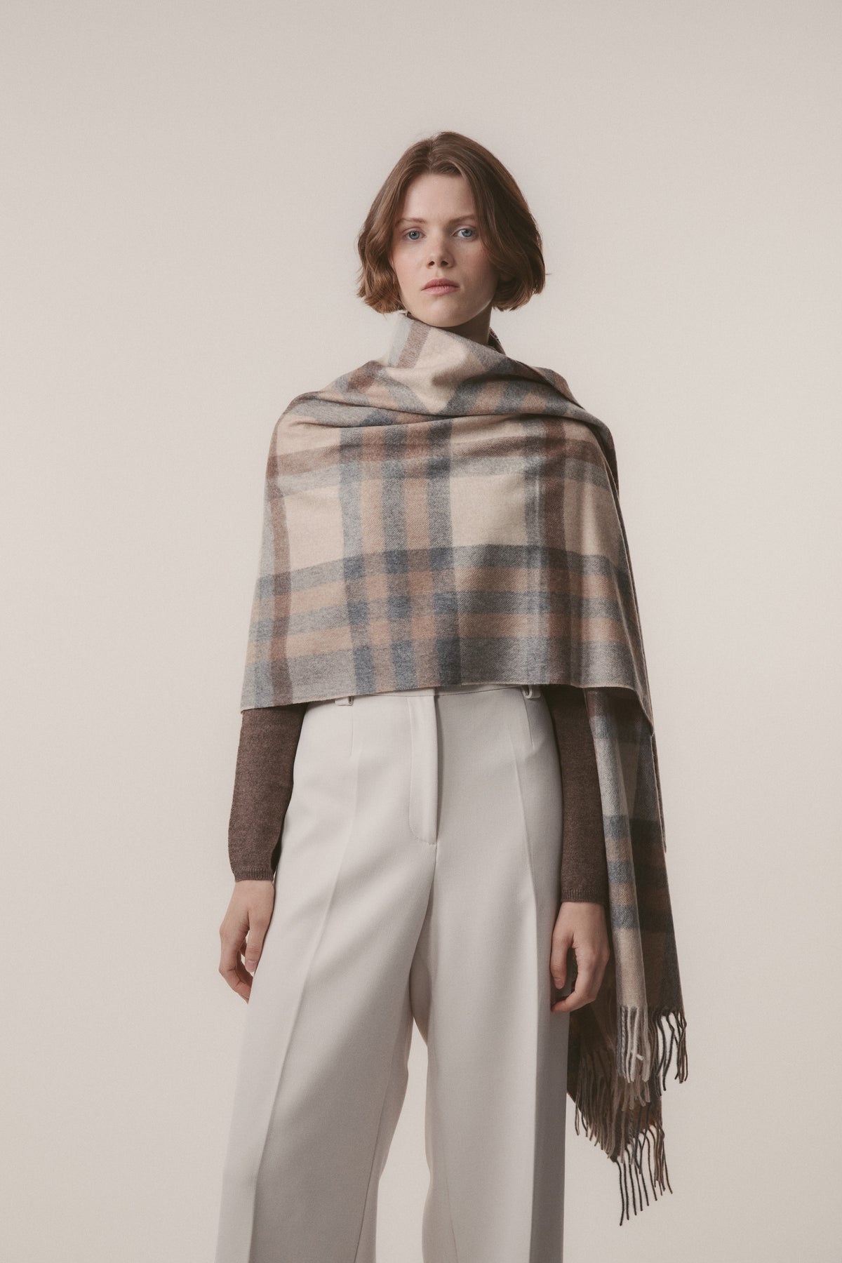 Model wearing Tartan 2 Cashmere Stole in Natural draped over shoulders, showing full plaid pattern in beige, blue, and brown with fringe detail