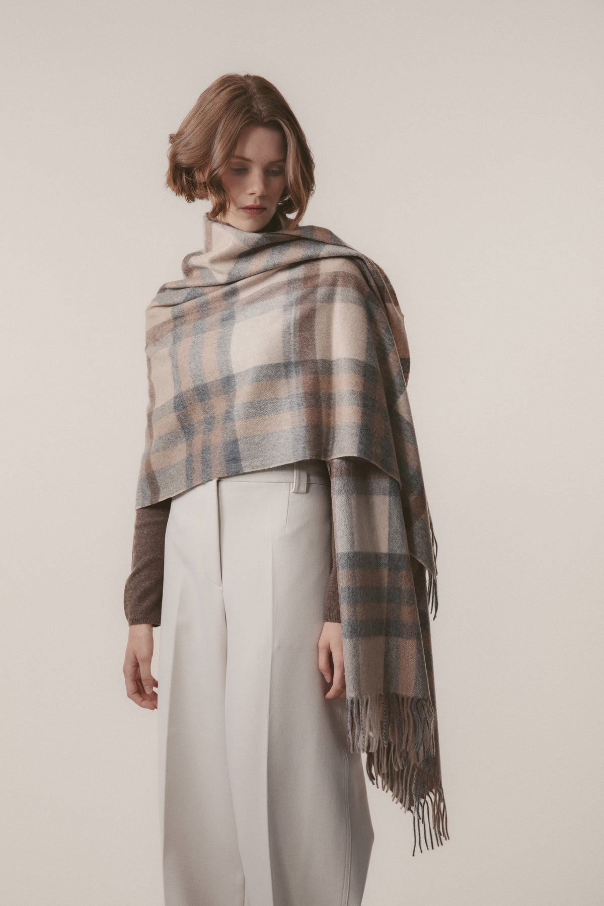 Model wearing Tartan 2 Cashmere Stole in Natural draped over shoulders, showing full plaid pattern with fringed ends