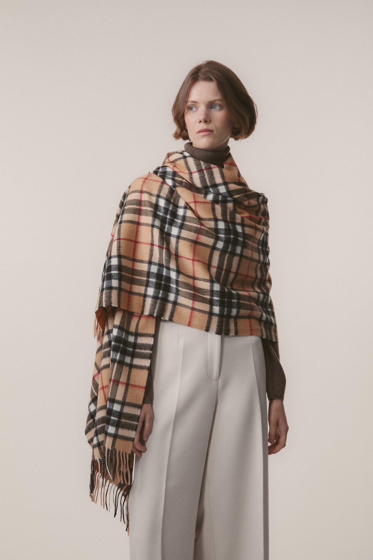 Model wearing Scotty Thompson Cashmere Stole in Camel draped over shoulders, showing tartan pattern with fringed edges