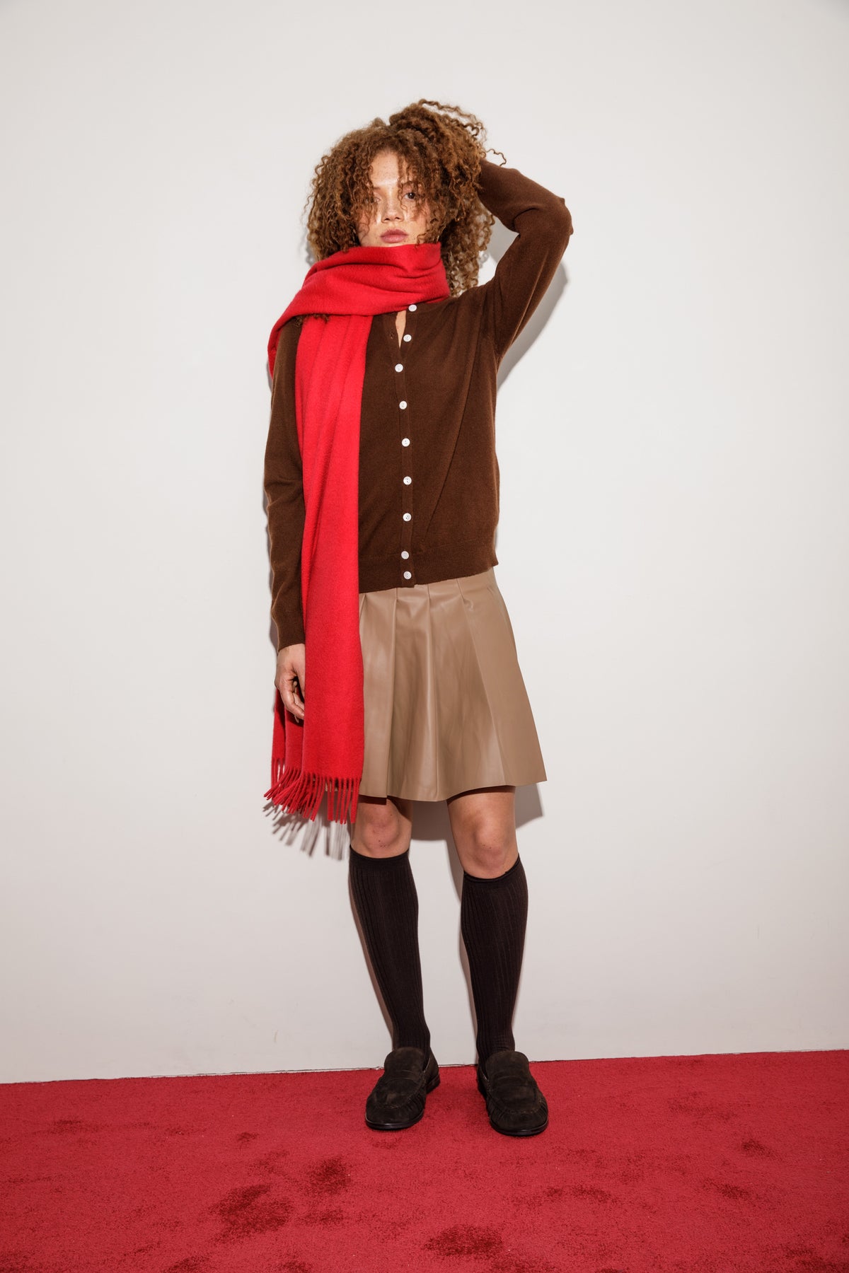 Solid Cashmere Wide Scarf in red draped over one shoulder, styled with a brown cardigan and pleated skirt, showing fringed ends
