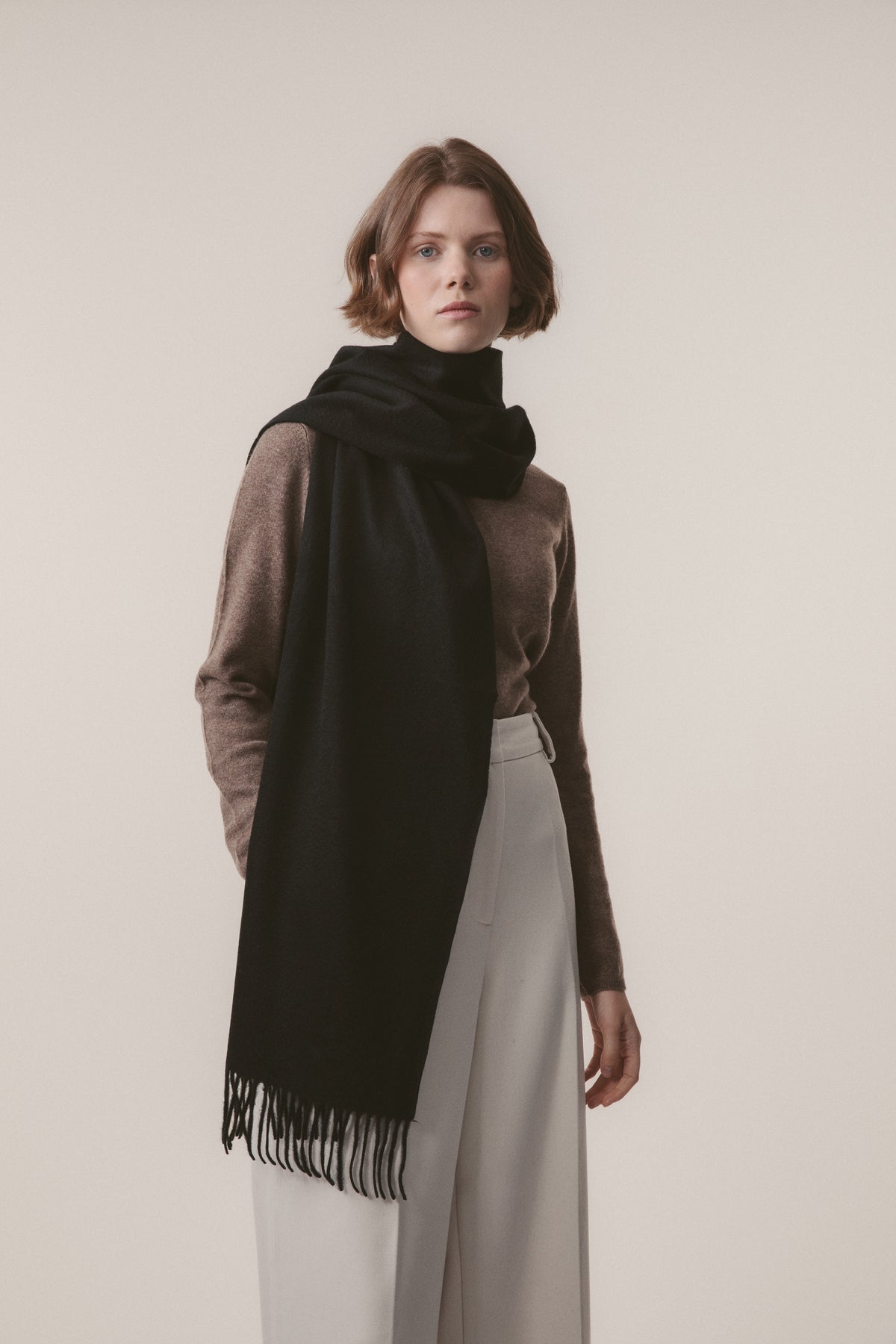 Woman wearing a black scarf over a brown sweater on a plain background