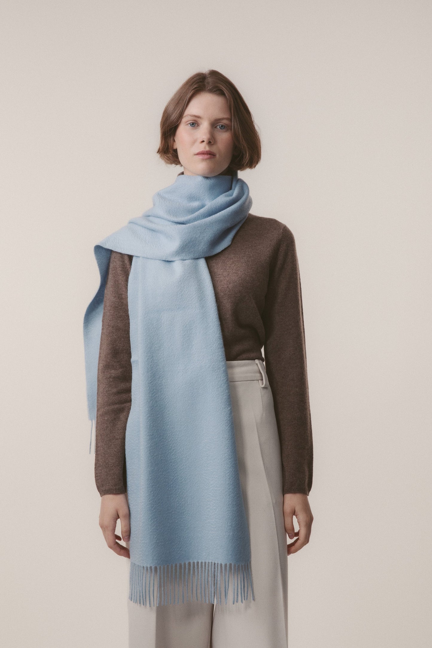 Solid Cashmere Wide Scarf in light blue with fringed ends, worn draped around the neck over a brown sweater
