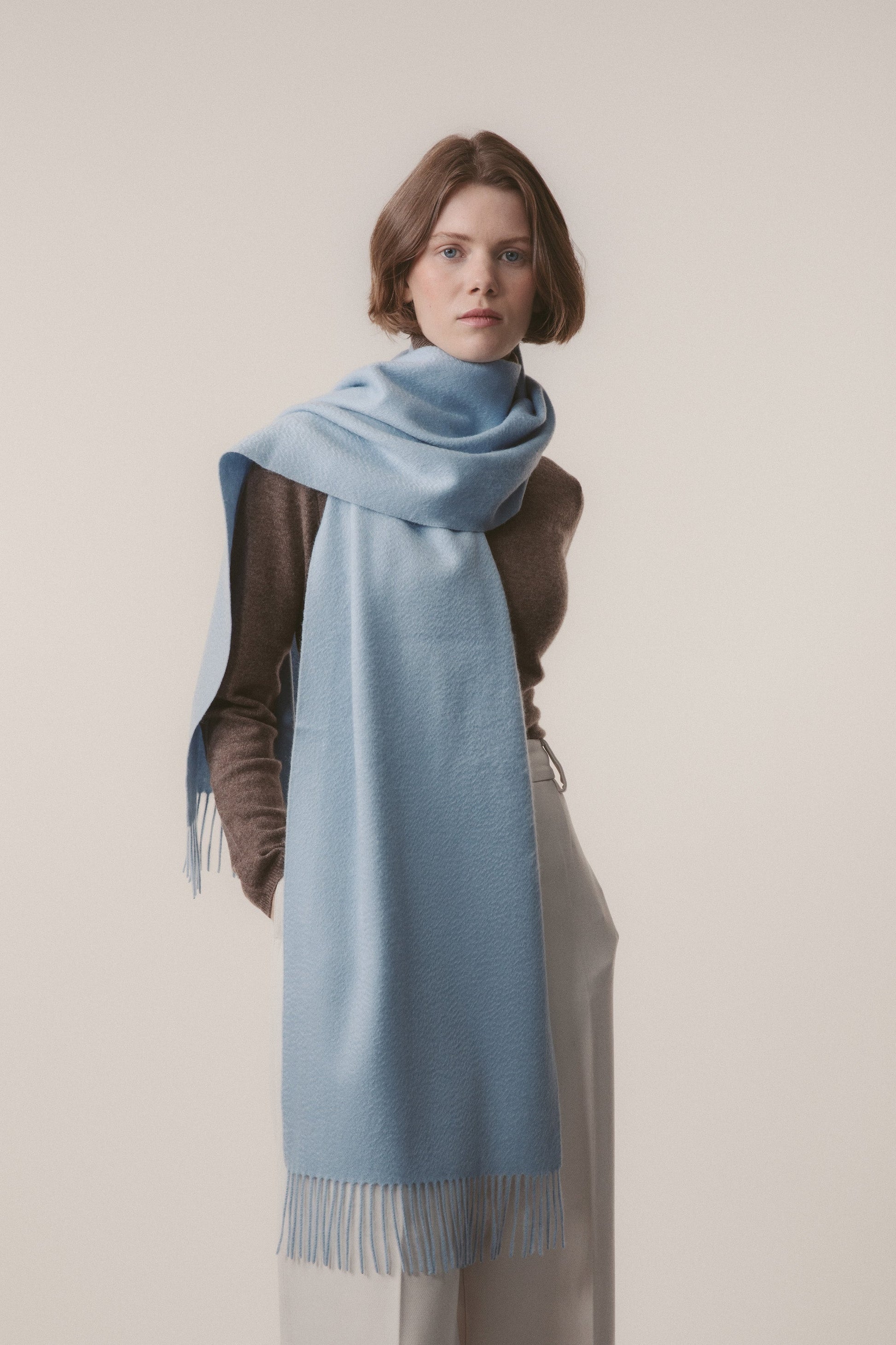 Solid Cashmere Wide Scarf in Blue styled draped around the neck with fringed ends visible, worn over a brown sweater