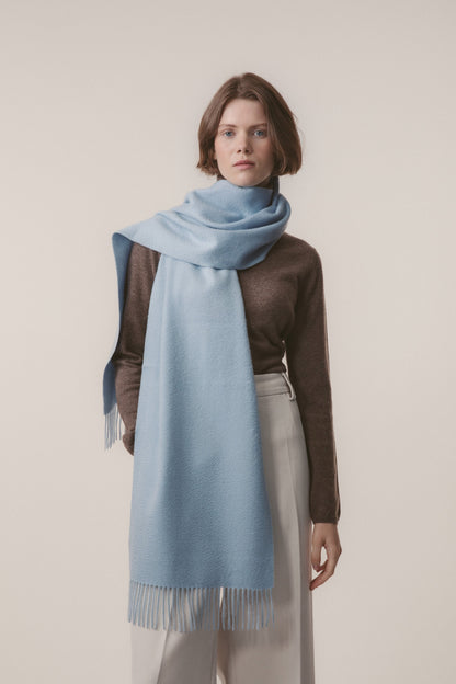 Solid Cashmere Wide Scarf in Blue styled wrapped around the neck with fringed ends draping to the knee