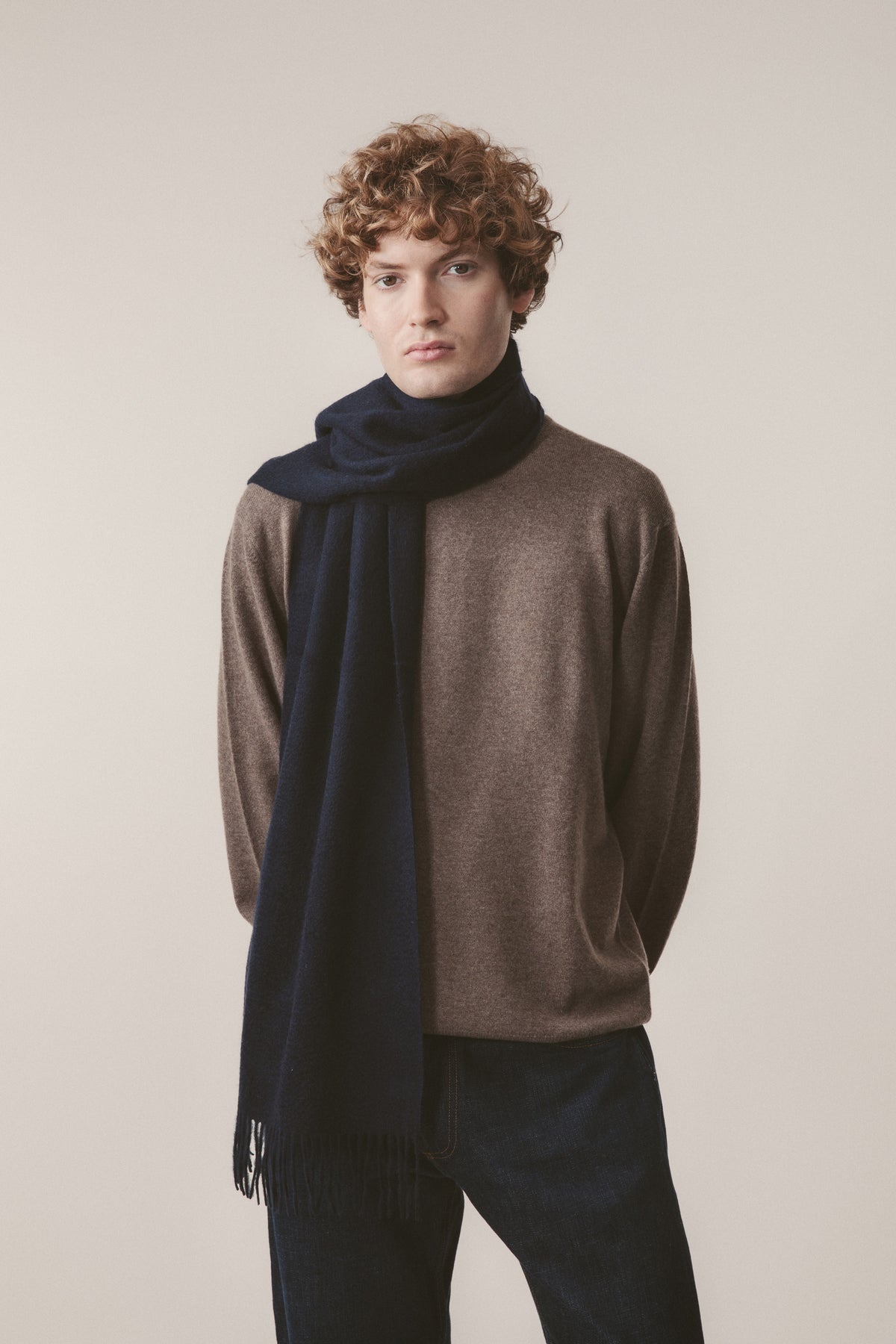 Solid Cashmere Wide Scarf in Dark Navy with fringed ends, styled draped over a brown sweater on a male model