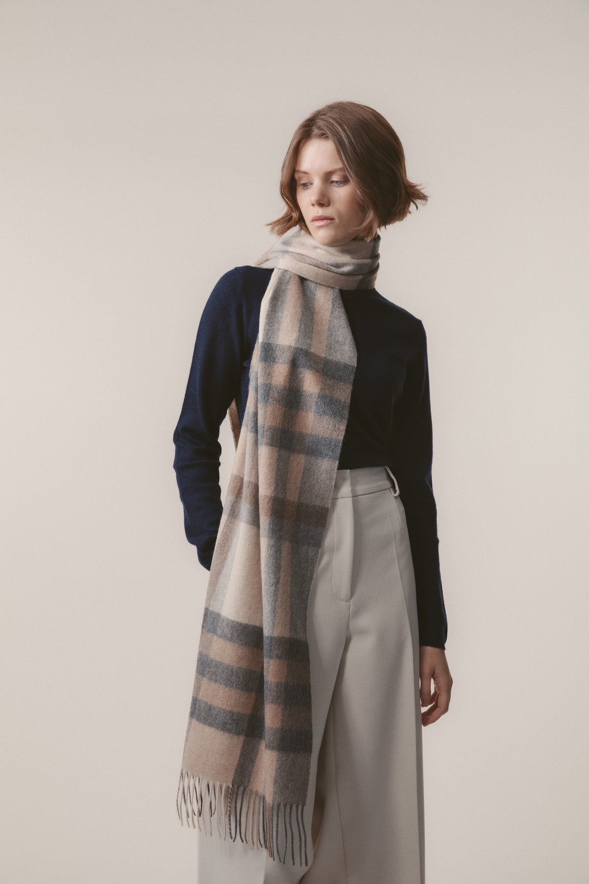 Tartan 2 Cashmere Wide Scarf in Natural, worn draped around the neck showing beige, cream, and grey plaid pattern with fringed ends