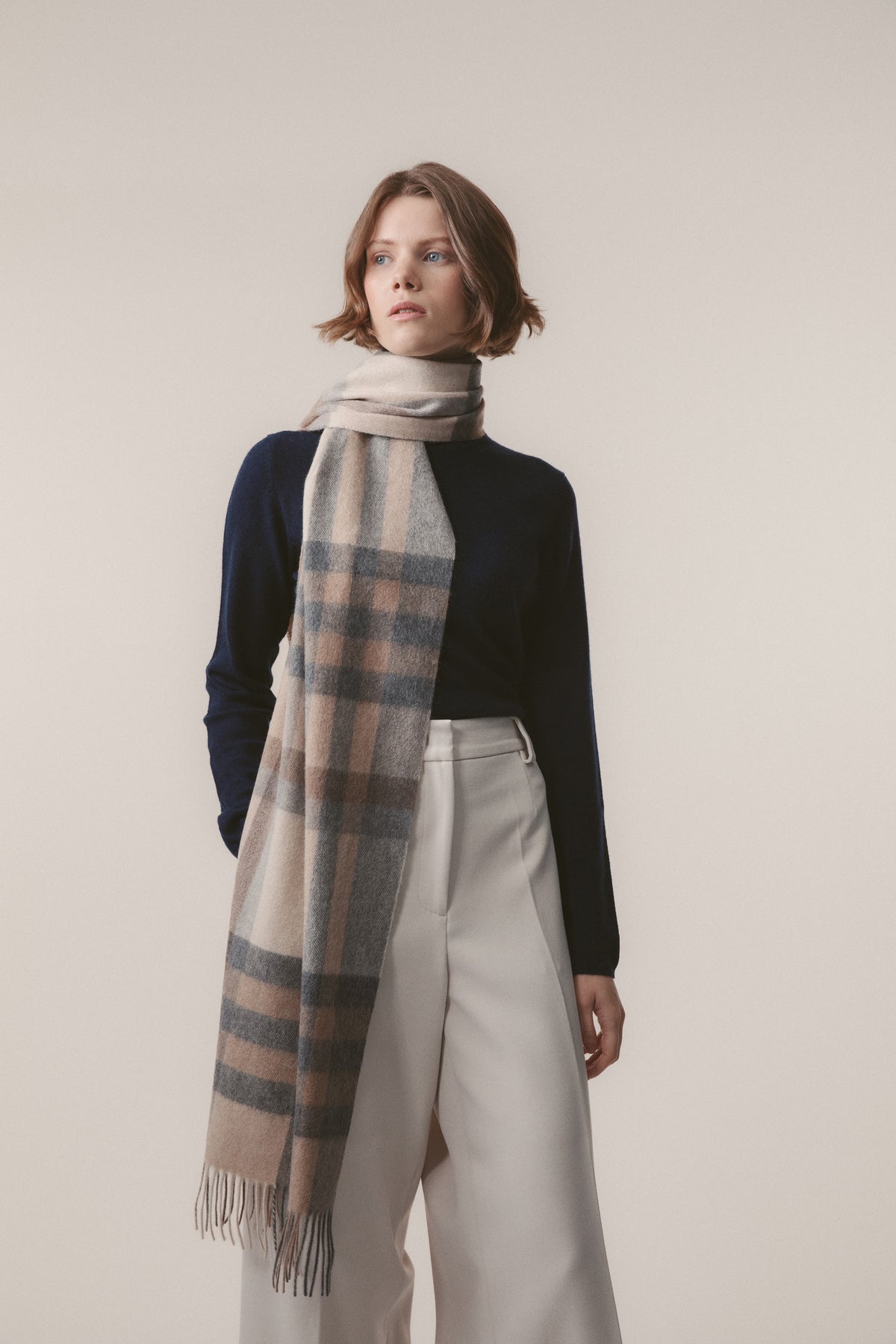 Tartan 2 Cashmere Wide Scarf in Natural worn looped around the neck, showing the beige and grey plaid pattern with fringed ends