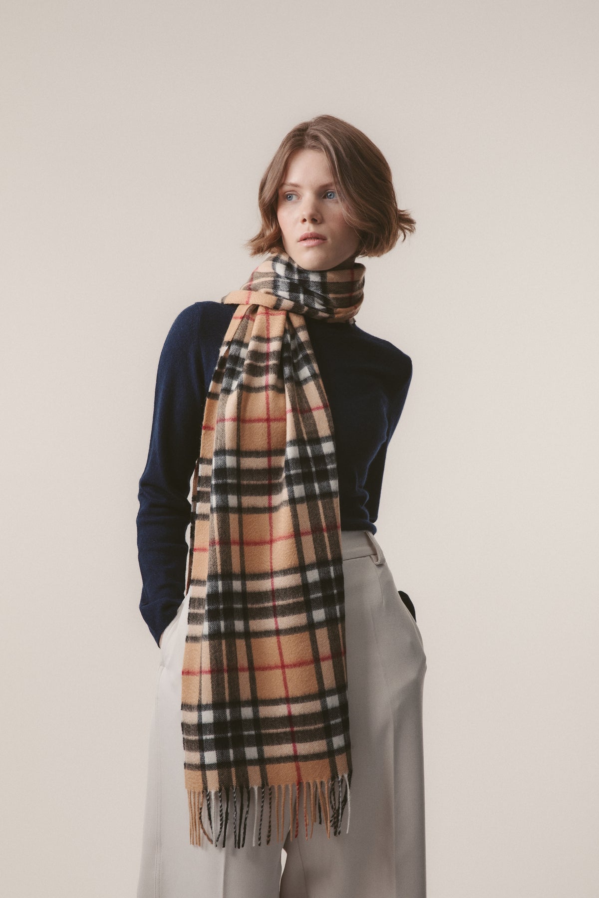 Scotty Thompson Cashmere Wide Scarf in Camel worn draped around the neck over a navy sweater, showing the full check pattern and fringe