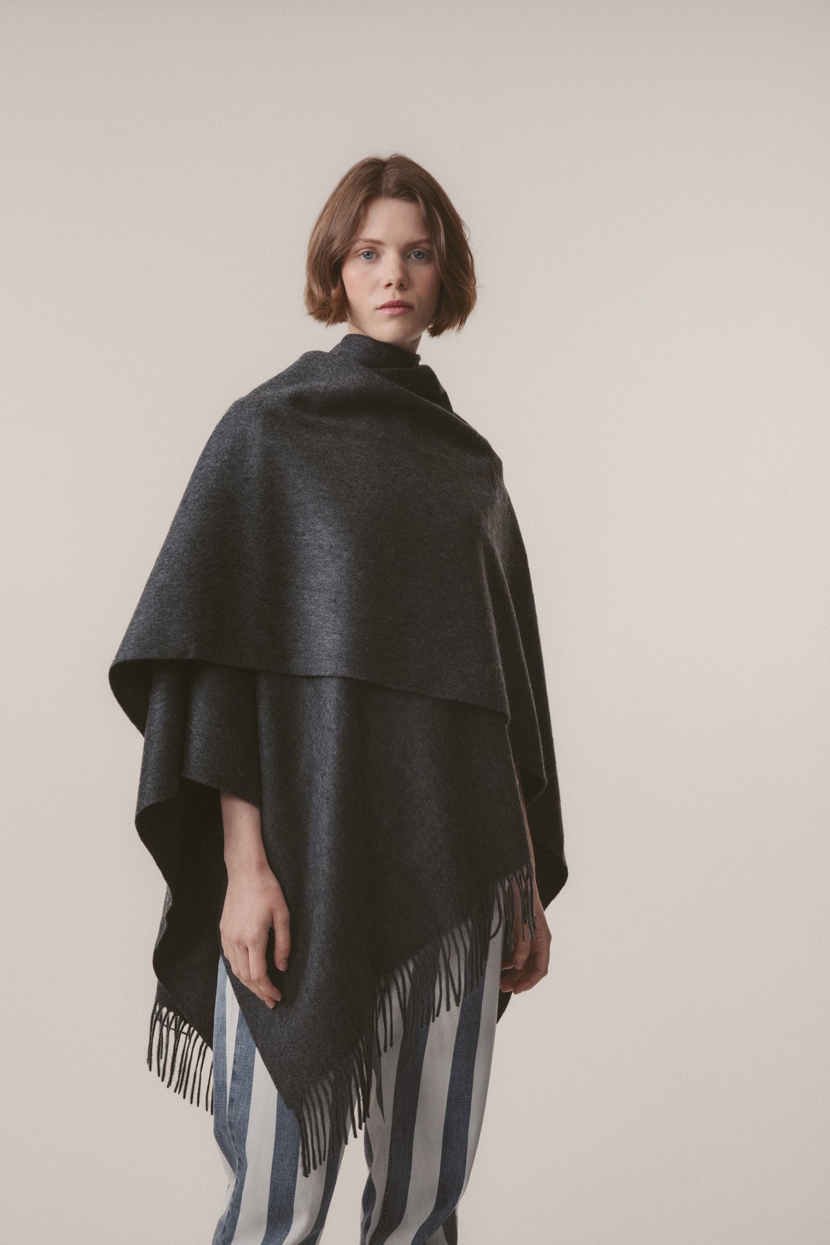 Model wearing Solid Cashmere Wrap in Steinway Grey draped over shoulders, showing fringed hem detail and layered draping
