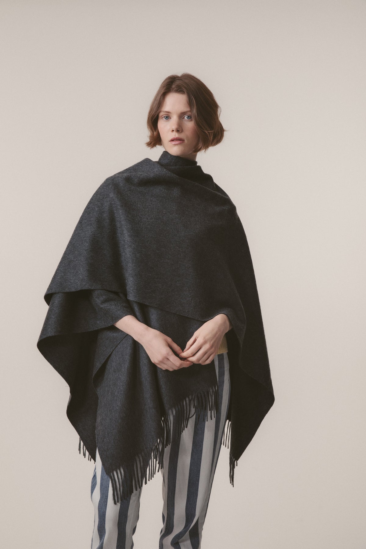 Model wearing Solid Cashmere Wrap in Steinway Grey draped as a poncho, showing fringed hem and relaxed drape