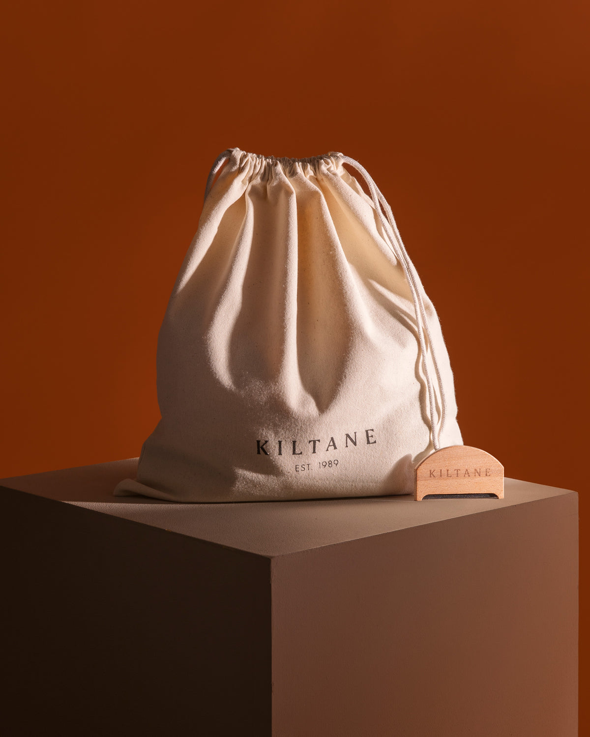 Kiltane Small Dustbag & Cashmere Comb — natural cotton drawstring bag with wooden comb beside it on a display plinth