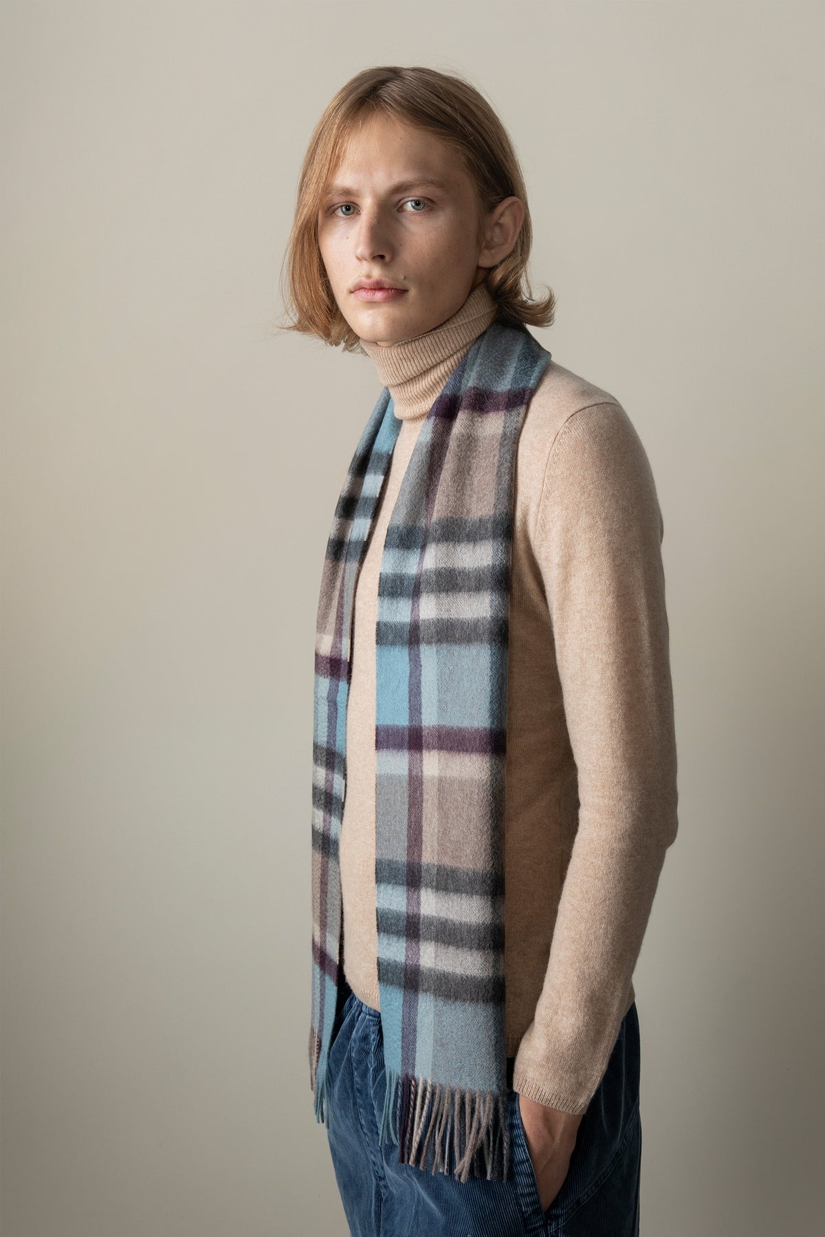 Tartan 2 Cashmere Scarf in Blue Taupe worn draped over a camel turtleneck, showing the plaid pattern and fringed ends