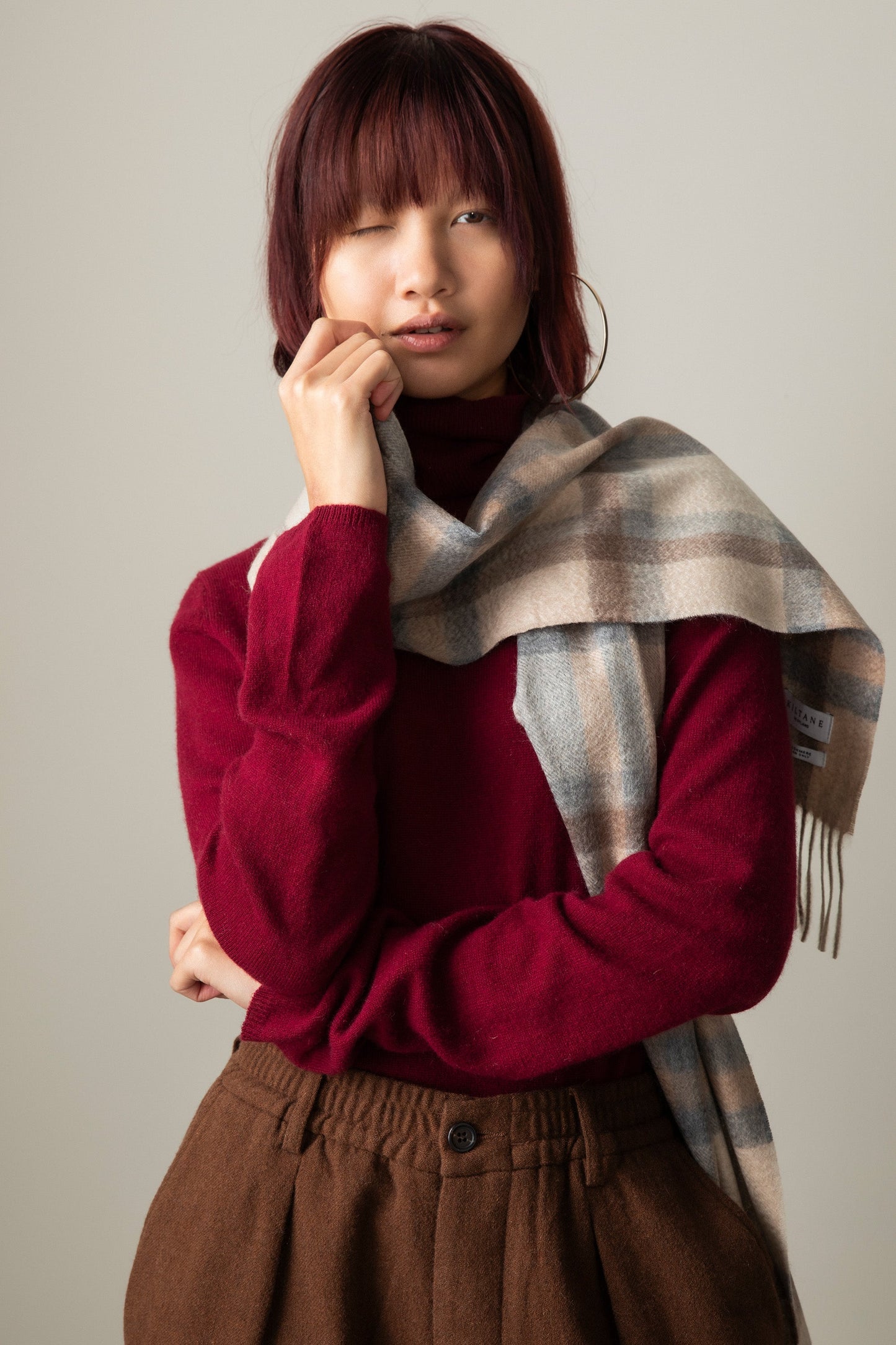 Tartan 2 Cashmere Scarf in Natural draped over one shoulder, showing beige and grey plaid pattern with fringed ends