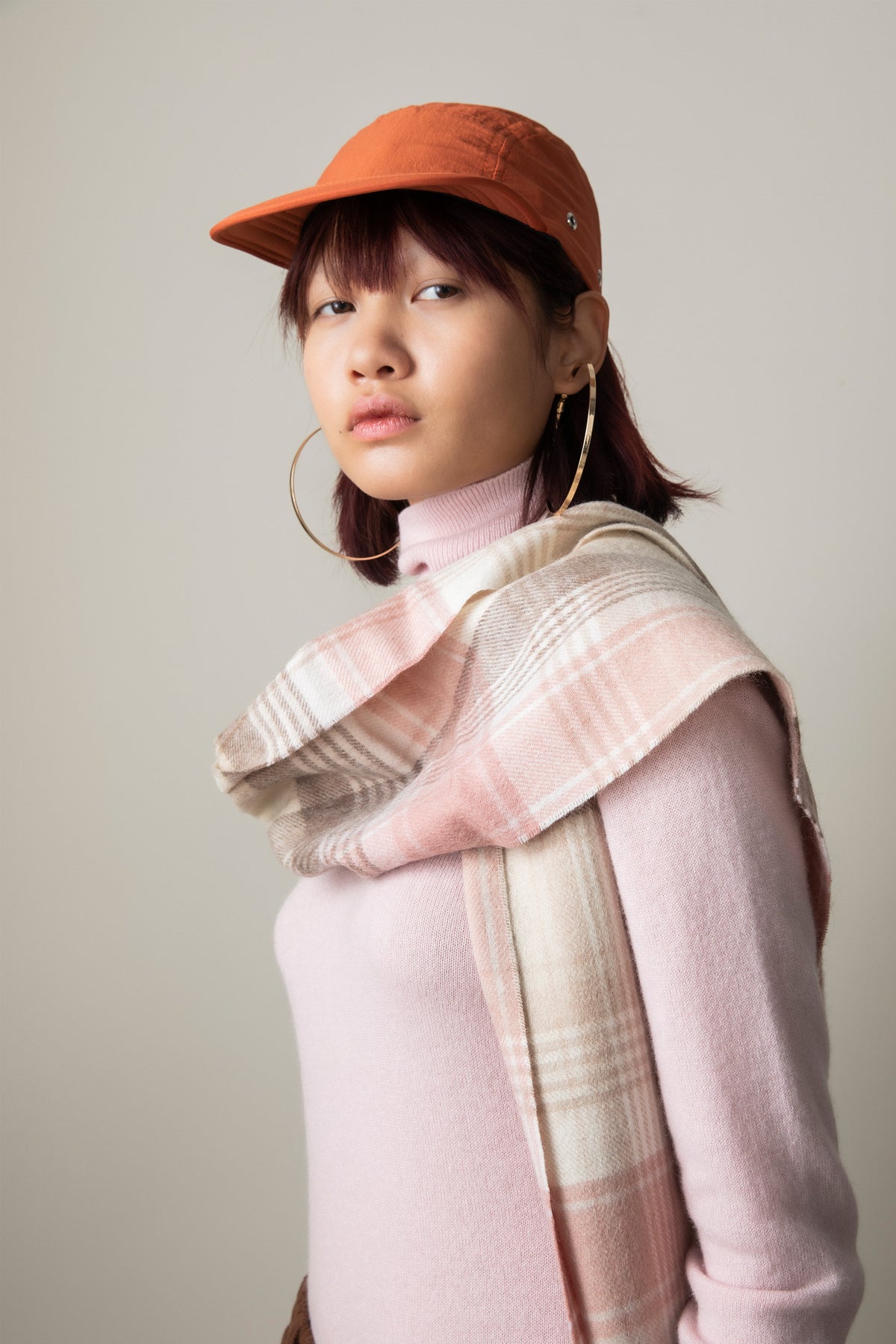 Repeat Edge Cashmere Scarf in Natural draped over one shoulder, showing pink and beige plaid pattern styled with a pink turtleneck