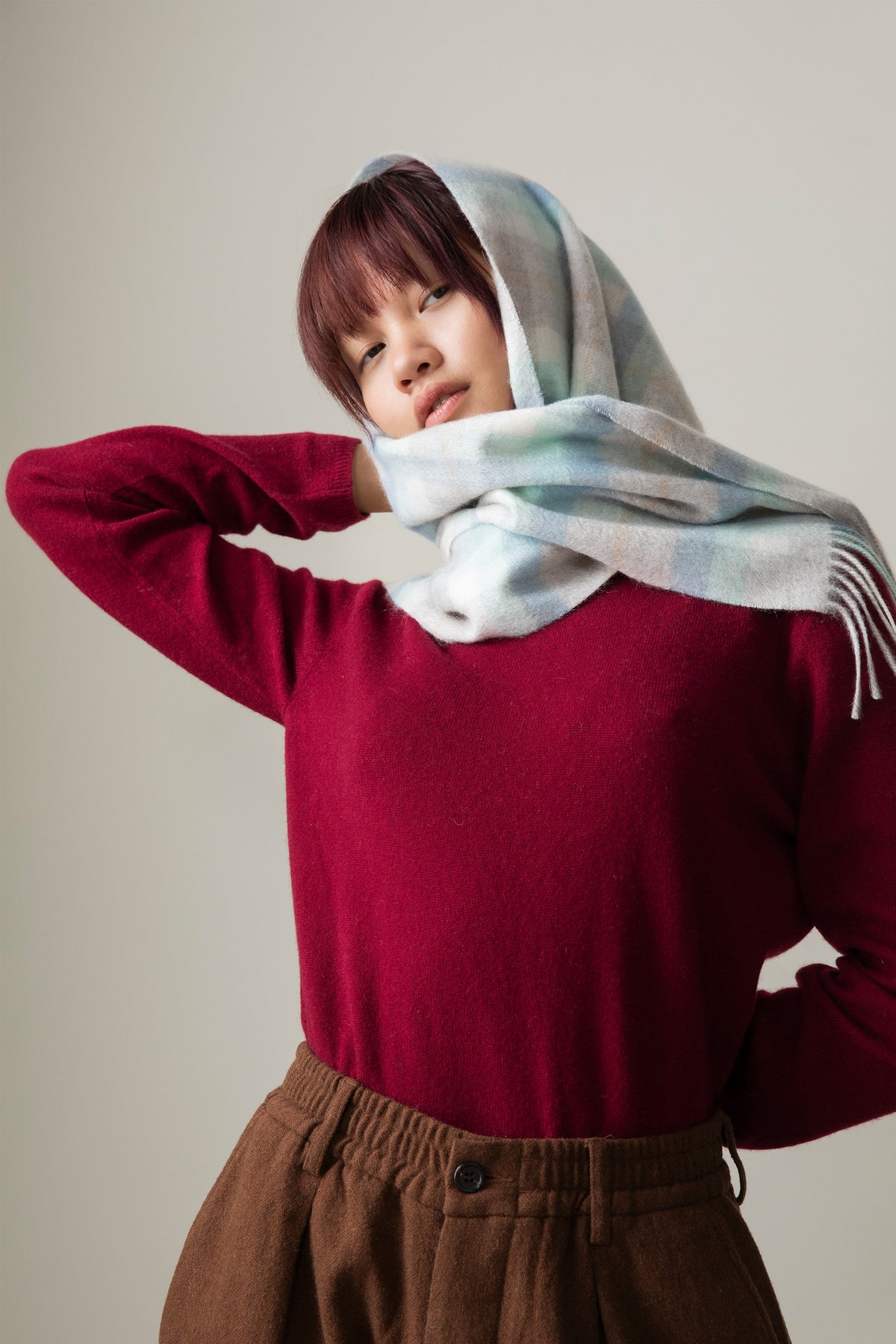 Contemporary Check Cashmere Scarf in Aqua worn as a headscarf, showing soft pastel check pattern and fringed edges