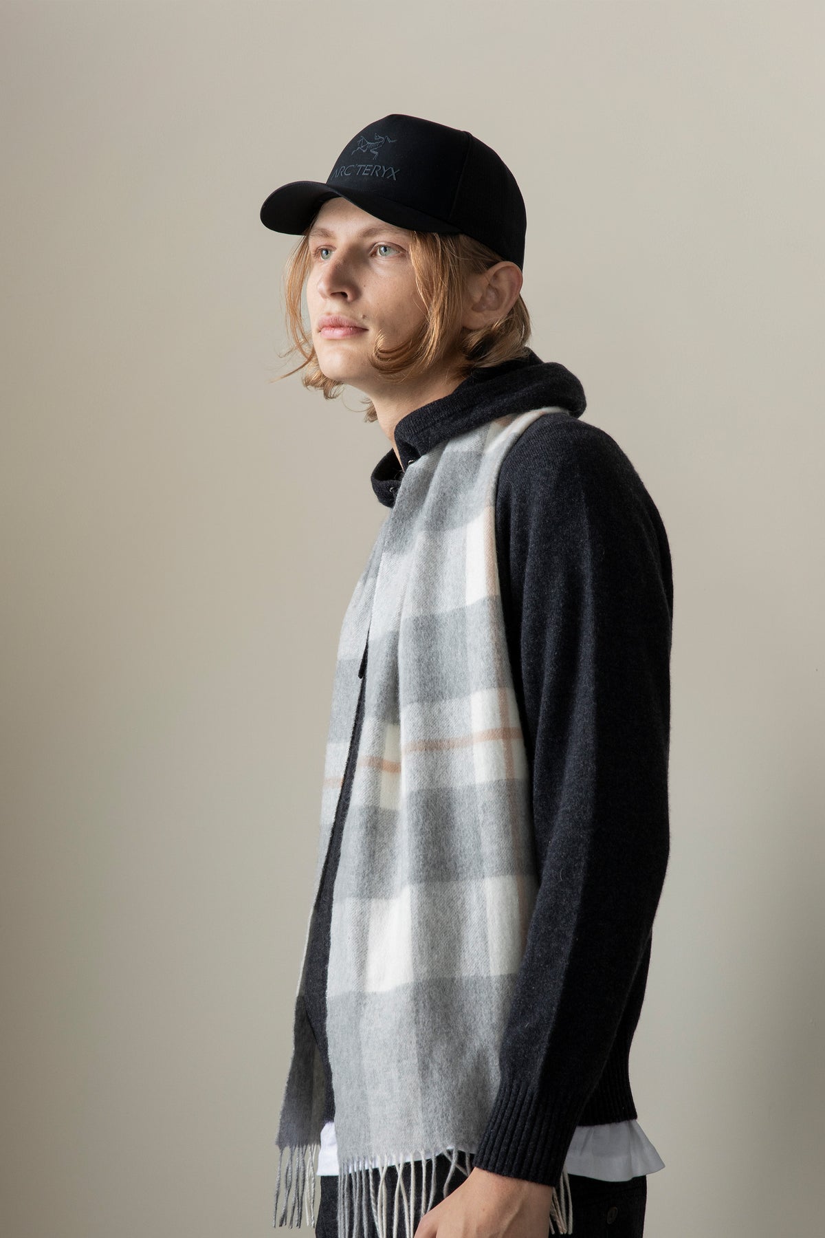 Contemporary Check Cashmere Scarf in Grey worn draped over a dark sweater, showing the plaid pattern and fringed ends