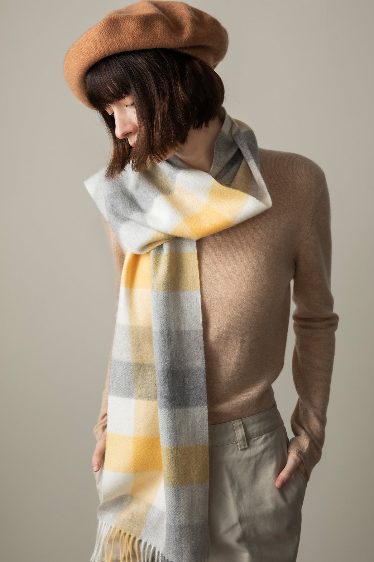 5 Square Check Cashmere Scarf in Butter worn loosely knotted over a camel sweater, showing the yellow, grey, and white plaid pattern