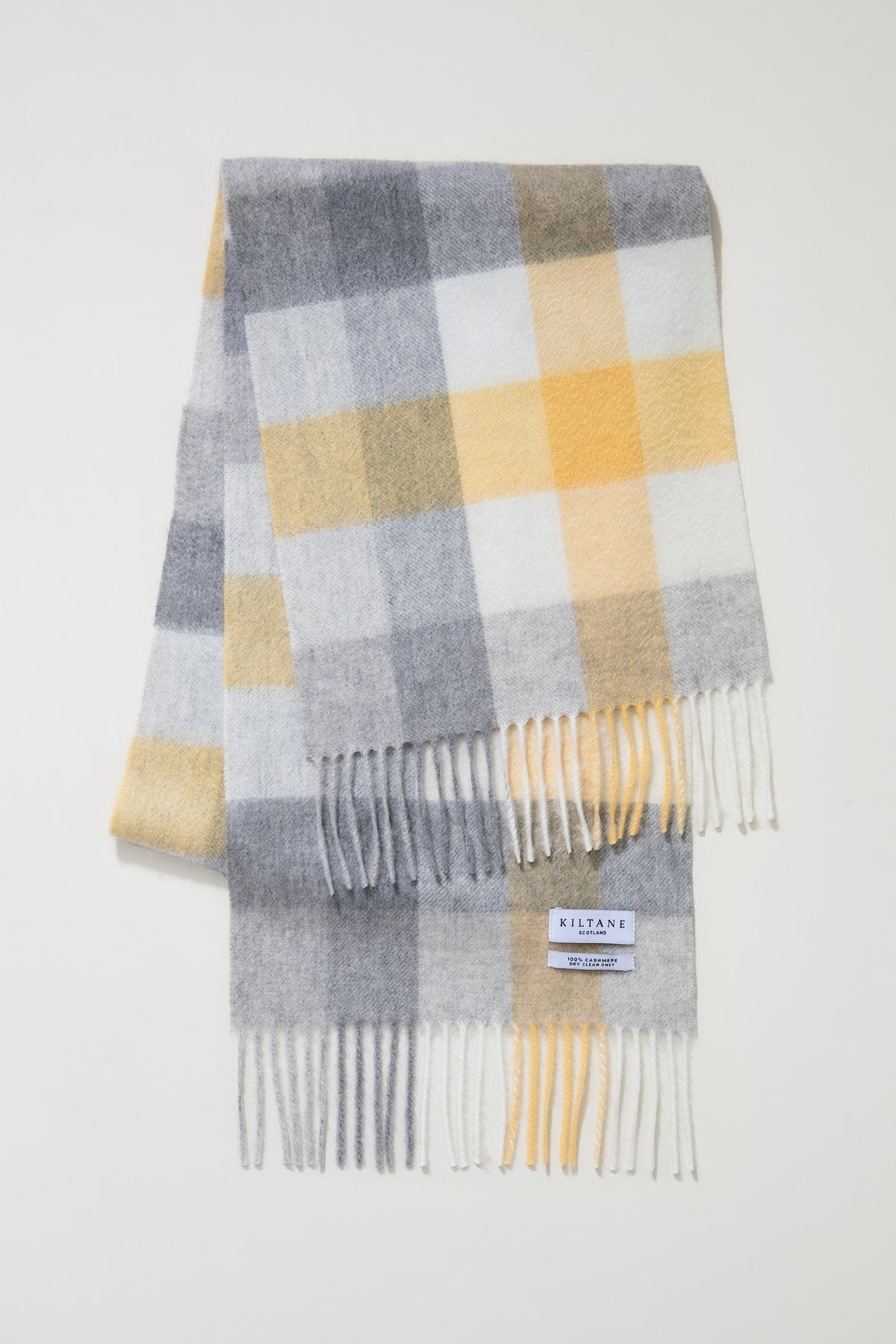 Kiltane 5 Square Check Cashmere Scarf in Butter folded flat showing brand label and fringed ends in grey, yellow, and white