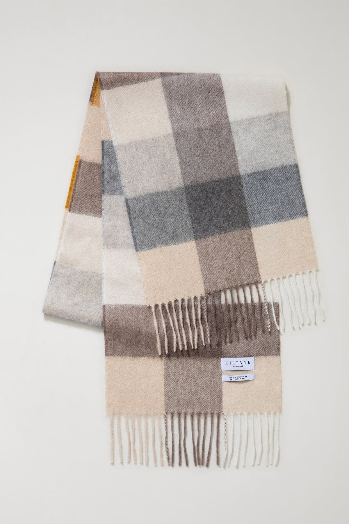 3 Square Cashmere Scarf in Gold colourway folded flat showing Kiltane Scotland label and fringed ends in neutral tones