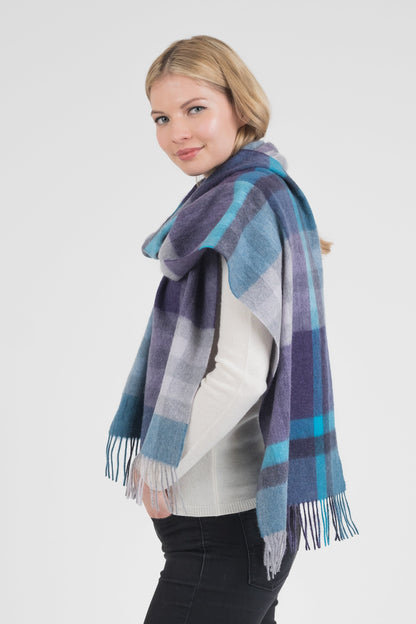 Model wearing Tartan 2 Cashmere Wide Scarf in Blue draped over shoulders, showing plaid pattern in purple, teal, and grey with fringed edges