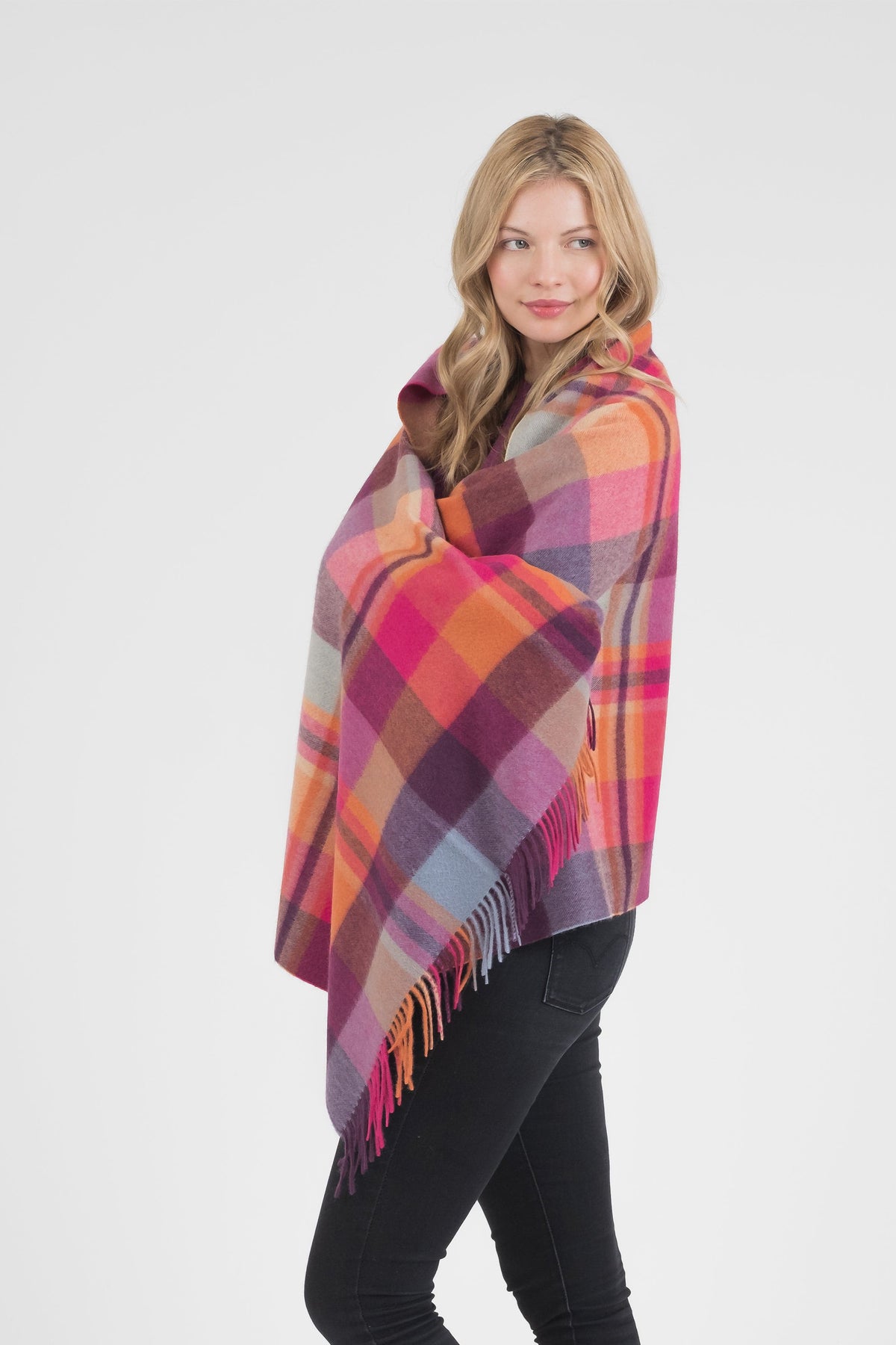 Model wrapping the Square Check Cashmere Stole in Orient Ginger around her shoulders, showing the pink, orange, and purple plaid with fringed edges