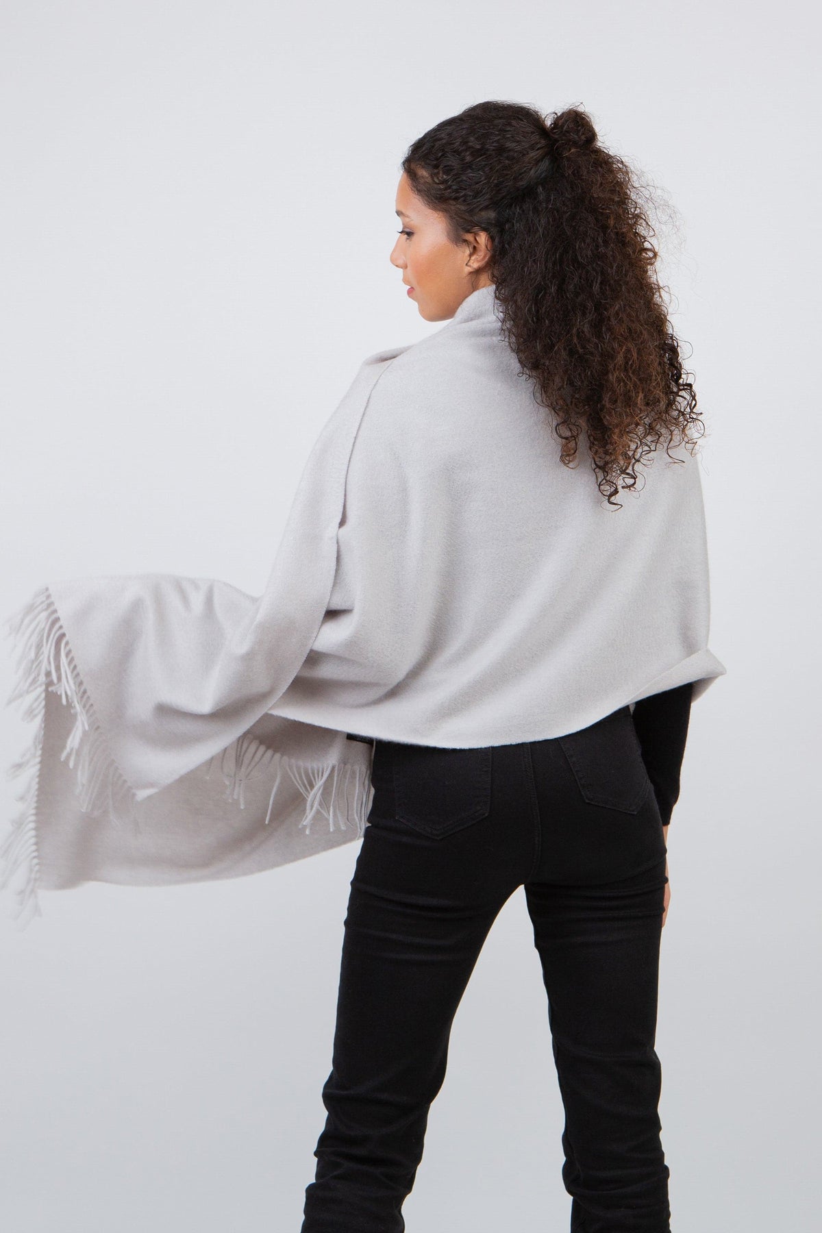 Back view of the Solid Cashmere Stole in Potash, showing the light grey wrap draped over shoulders with fringed edges flowing
