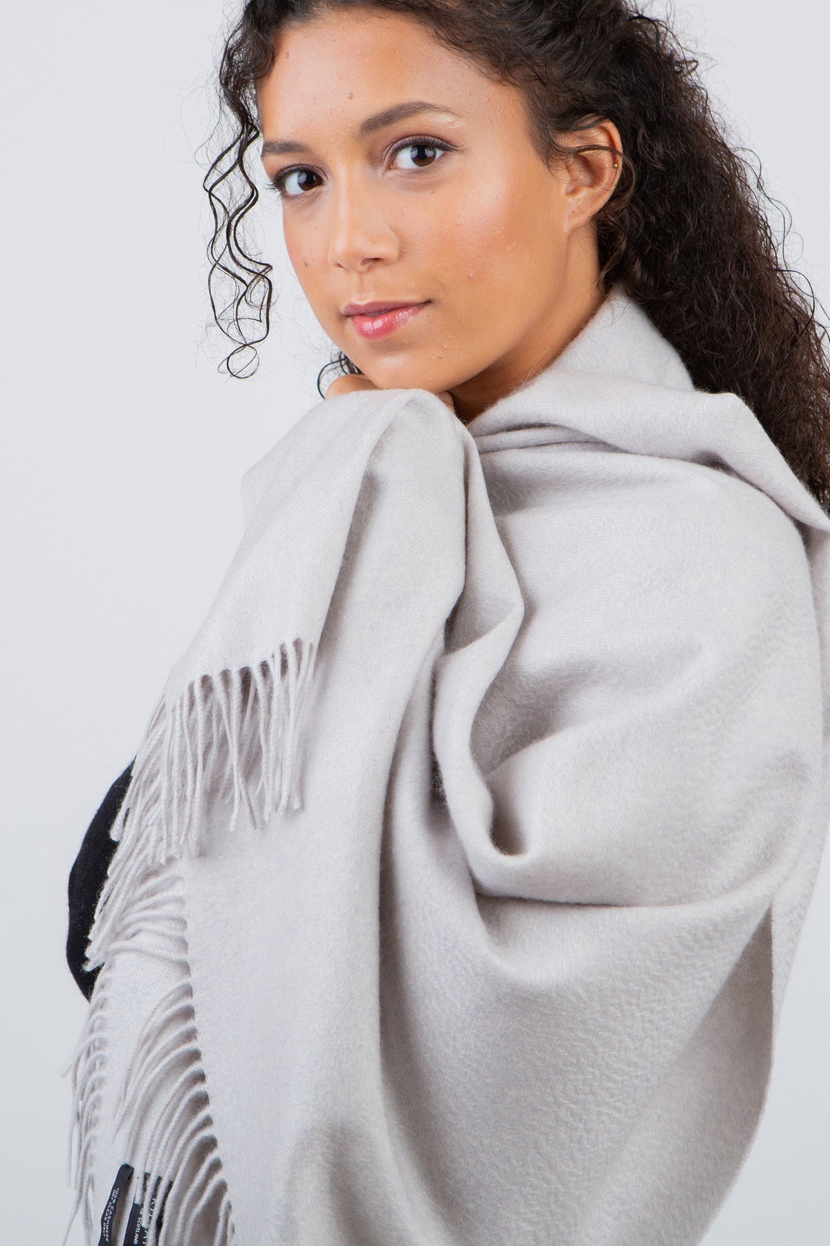 Solid Cashmere Stole in Potash worn wrapped around shoulders, showing soft grey fabric texture and fringed edge detail