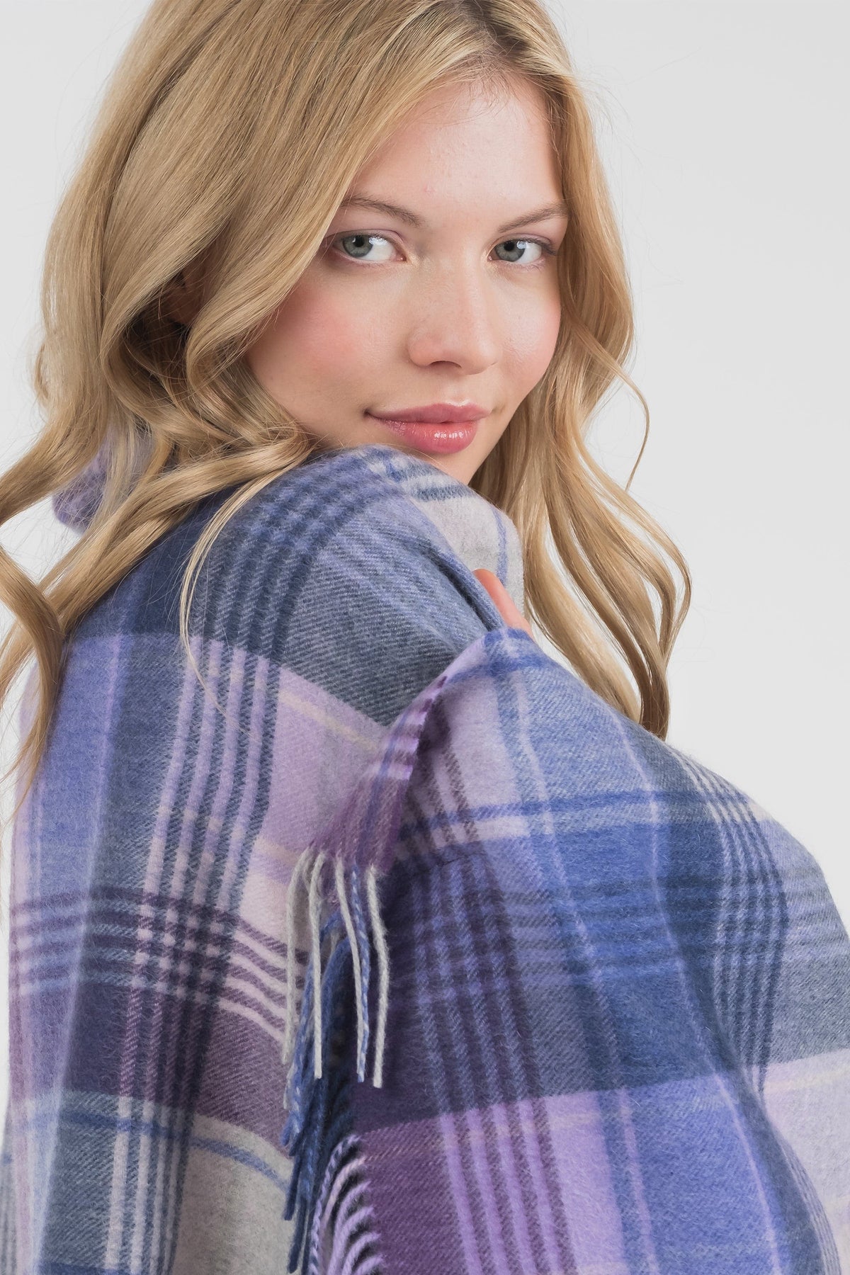Model wrapping Repeat Edge Cashmere Stole in Purple around her shoulder, showing soft tartan weave and fringed edge detail