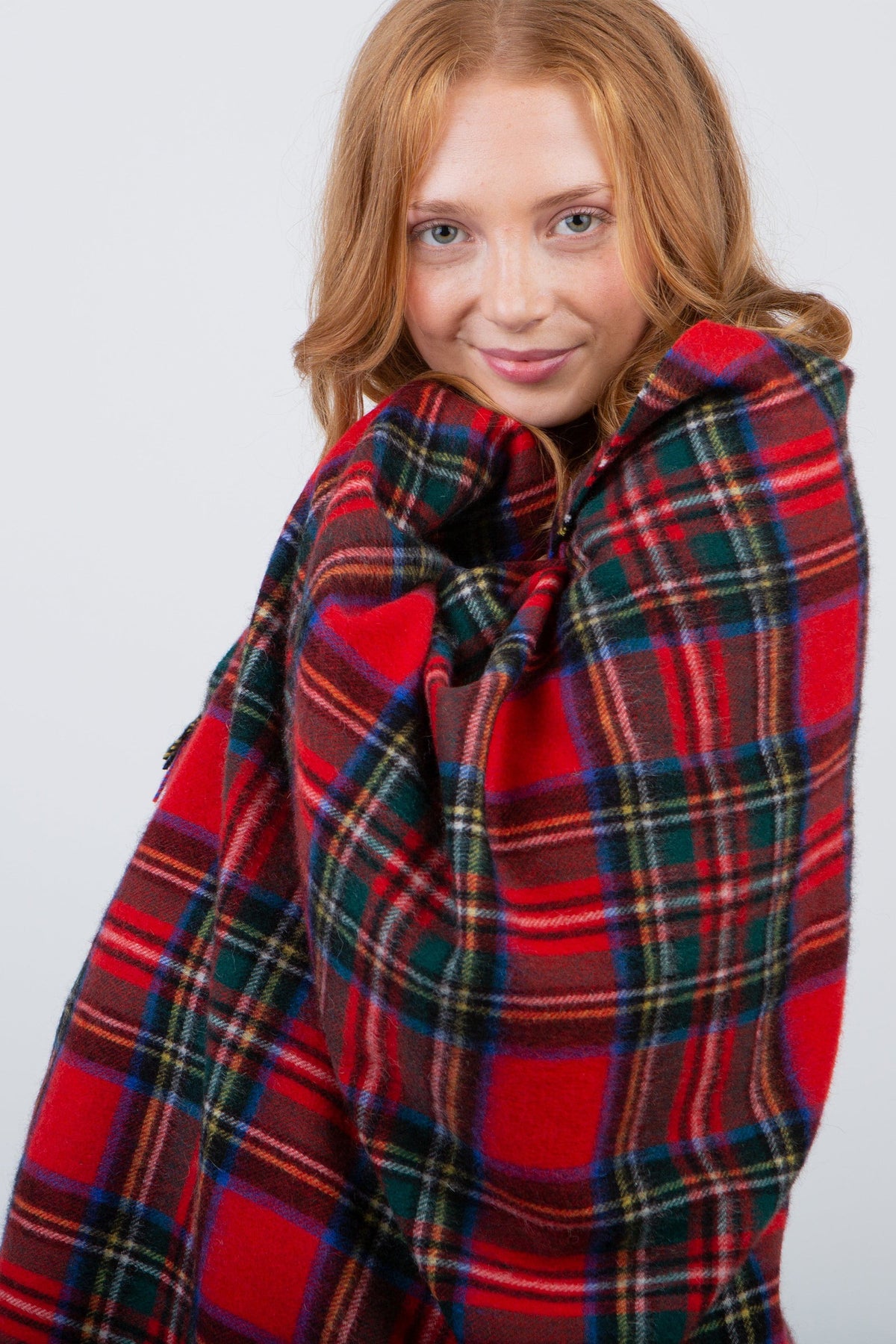 Model wrapping Heritage Tartan Cashmere Stole in Royal Stewart pattern snugly around her shoulders, showing soft wool texture