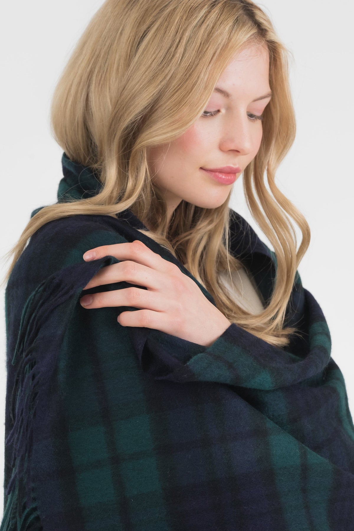 Model wrapping the Heritage Tartan Cashmere Stole in Blackwatch green and navy plaid, showing soft texture and fringed edge