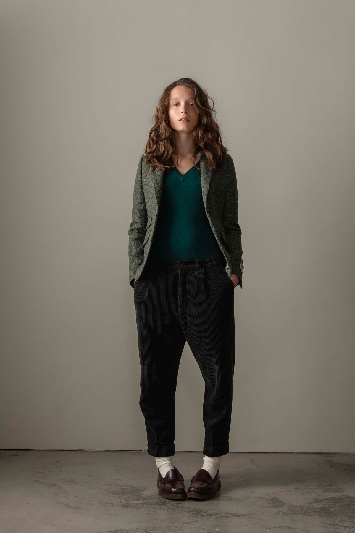 Women's Harris Tweed Janice Blazer in dark green herringbone worn open over a teal v-neck sweater with black corduroy trousers