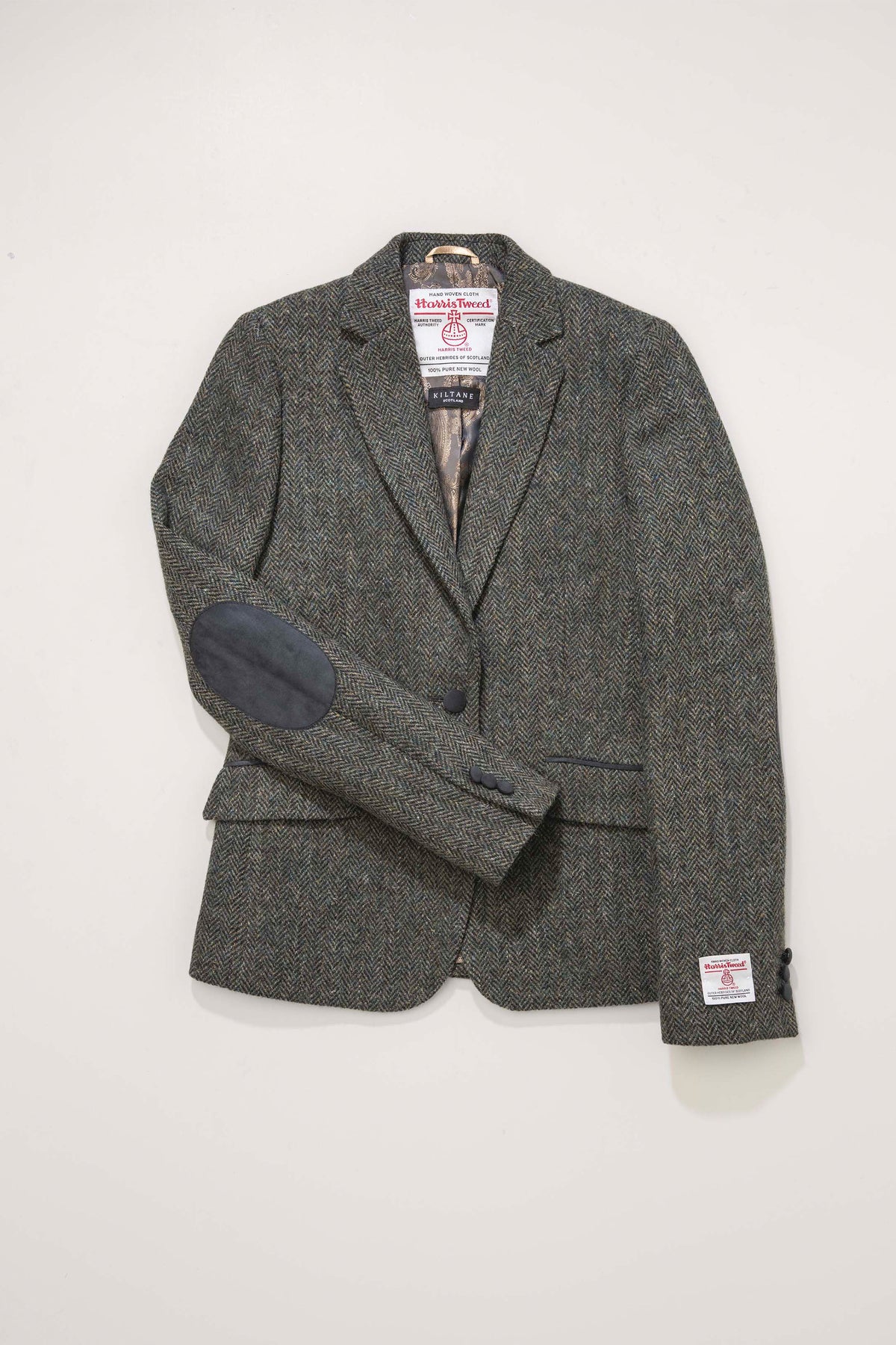 Women's Harris Tweed Janice Blazer in dark green herringbone laid flat, showing leather elbow patches and certification label