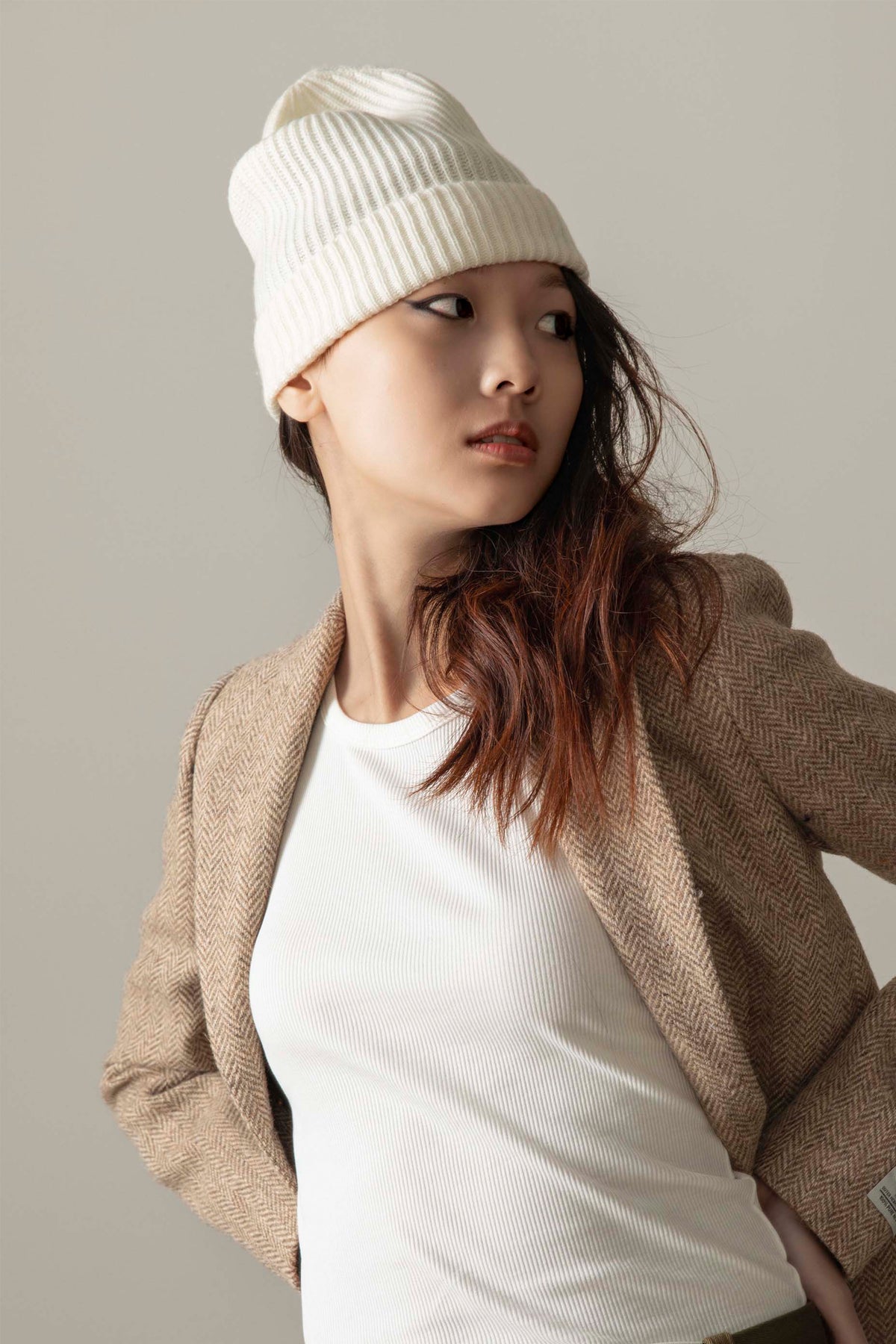 Unisex Cashmere Ribbed Beanie Hat in Soft White with folded cuff, worn by model styled with a herringbone blazer