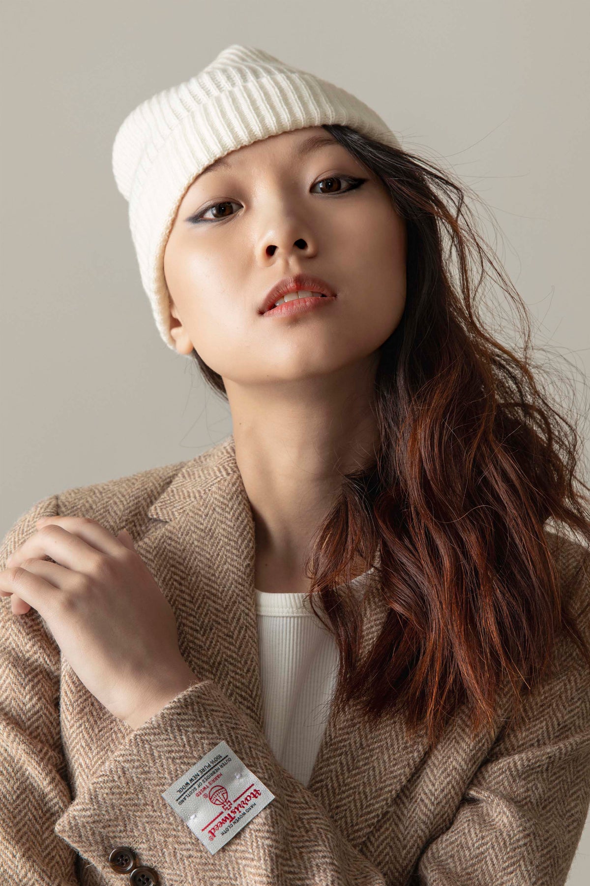 Unisex Cashmere Ribbed Beanie Hat in Soft White worn styled with a herringbone blazer, showing ribbed texture and relaxed fit