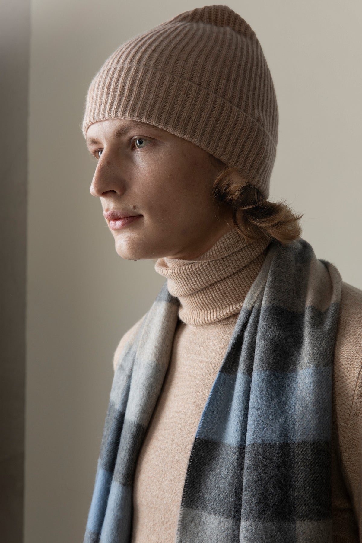 Unisex Cashmere Ribbed Beanie Hat in Sand, worn by model showing ribbed knit texture and folded cuff in a soft neutral tone