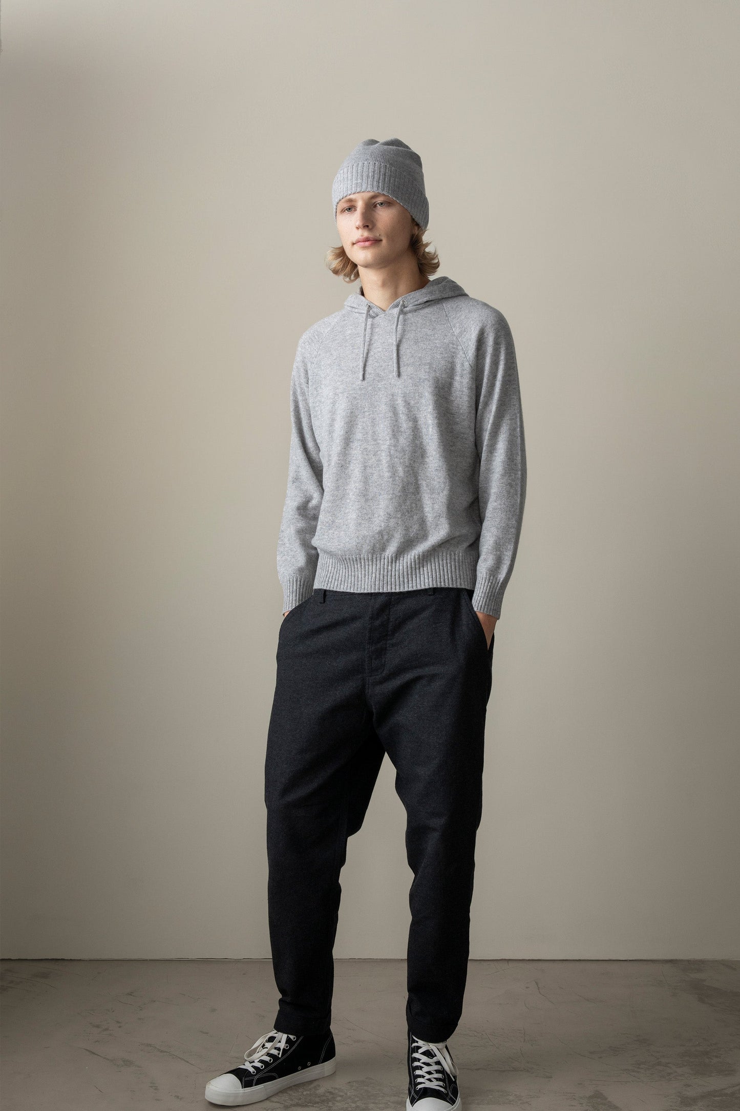 Model wearing the Unisex Cashmere Hoodie in Light Grey, full-length front view styled with dark trousers and a matching grey beanie