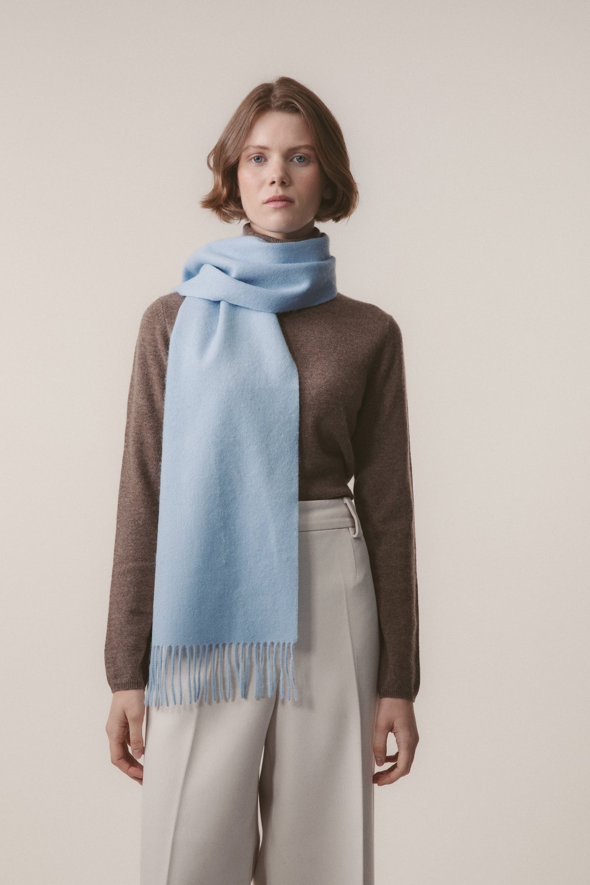 Solid Lambswool Scarf in Cashmere Blue with fringed ends, worn looped around the neck by a model in a brown sweater