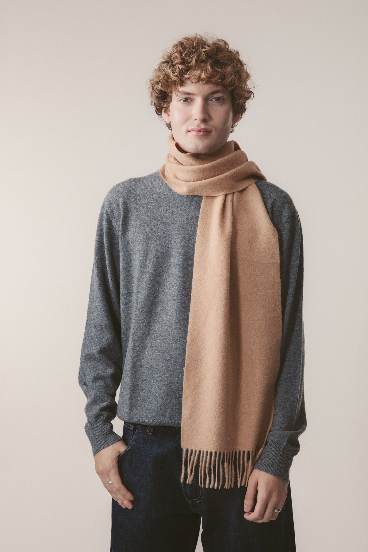 Solid Lambswool Scarf in Warm Camel worn looped around the neck with fringed ends, styled over a grey sweater