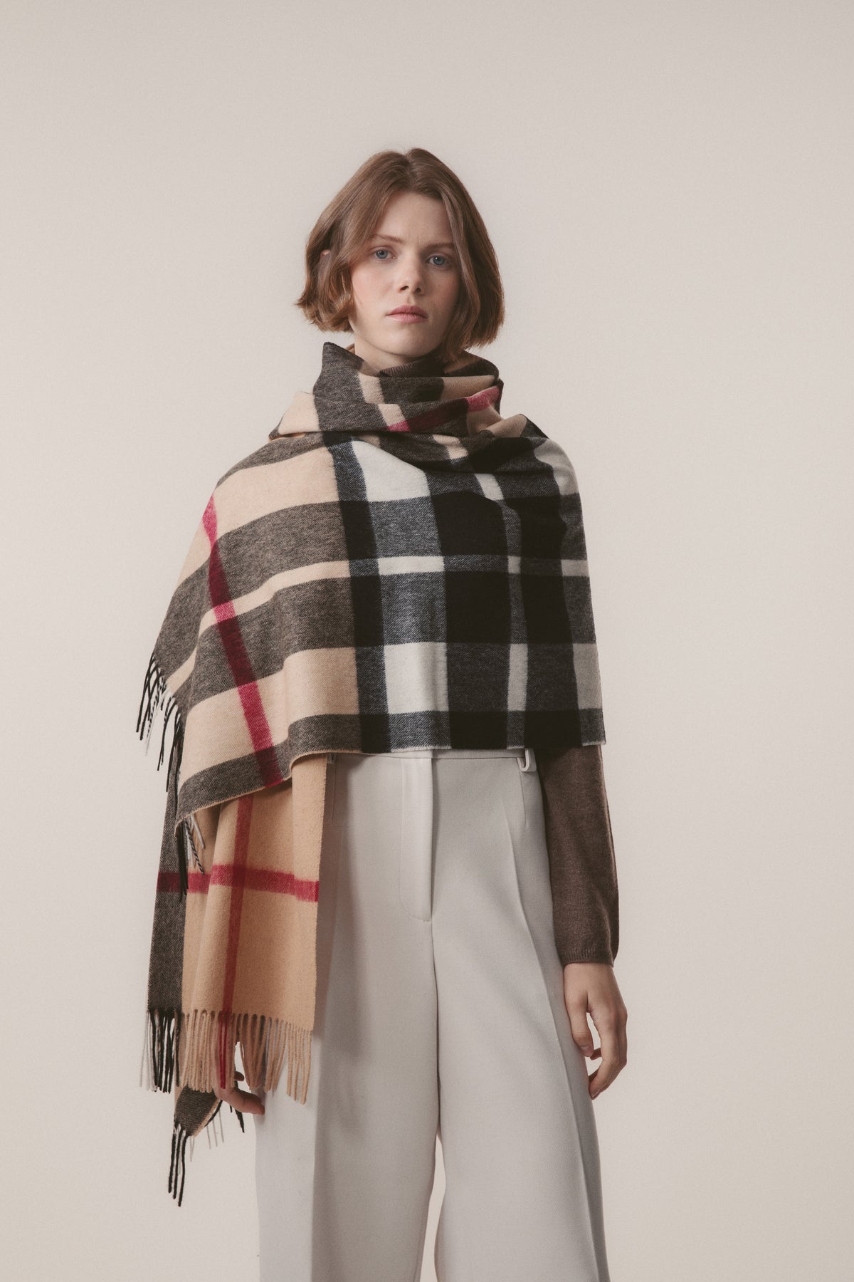 Model wearing Exploded Camel Thompson Lambswool Stole draped over shoulders, showing reversible beige and black check pattern with fringe