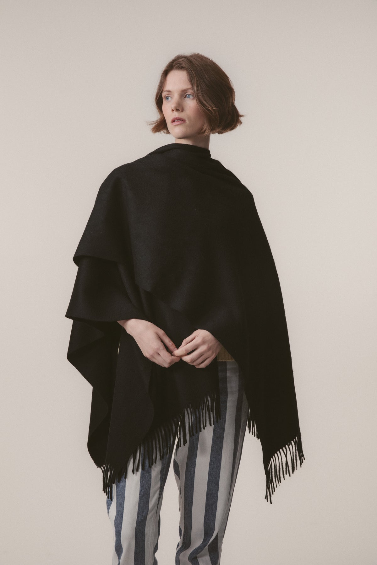 Model wearing Solid Lambswool Wrap in Black draped over shoulders, showing fringe detail along the hem
