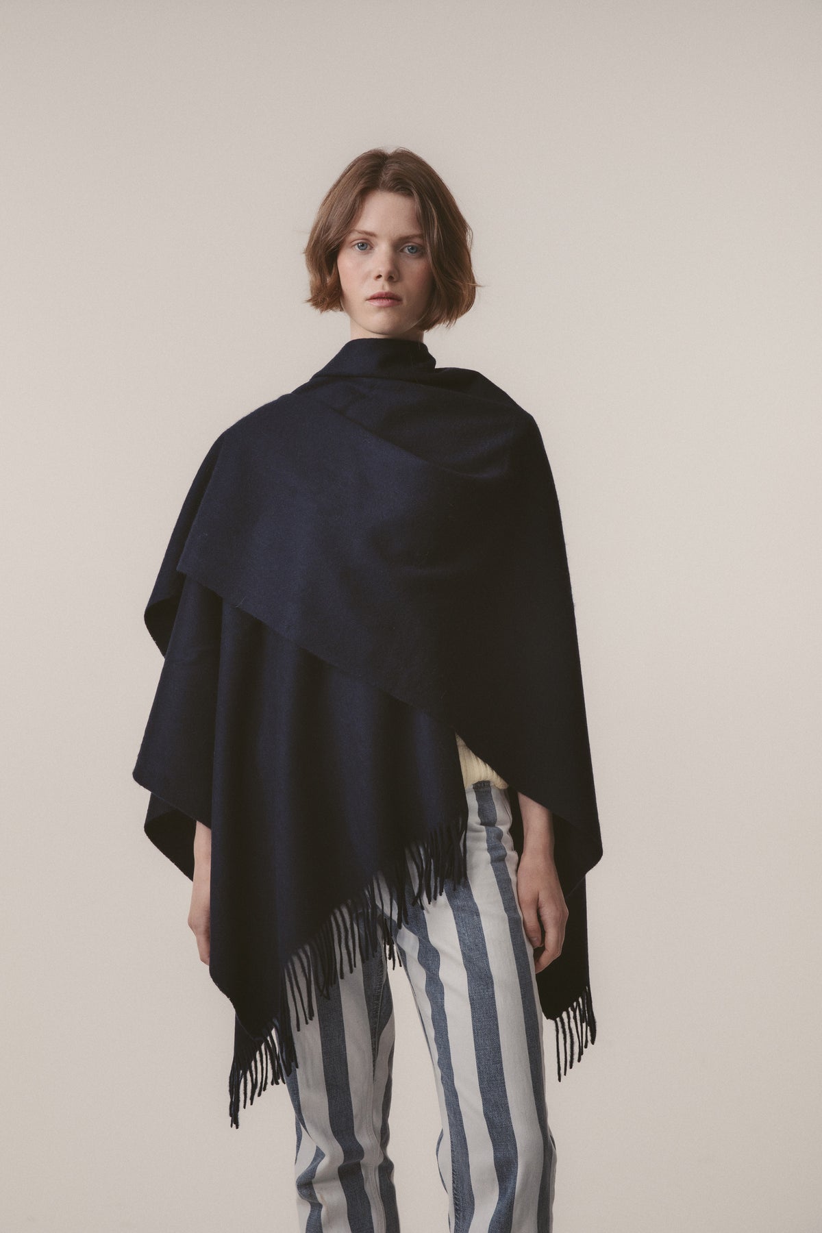 Model wearing Solid Lambswool Wrap in Dark Navy draped over shoulders, showing fringed hem detail and full drape