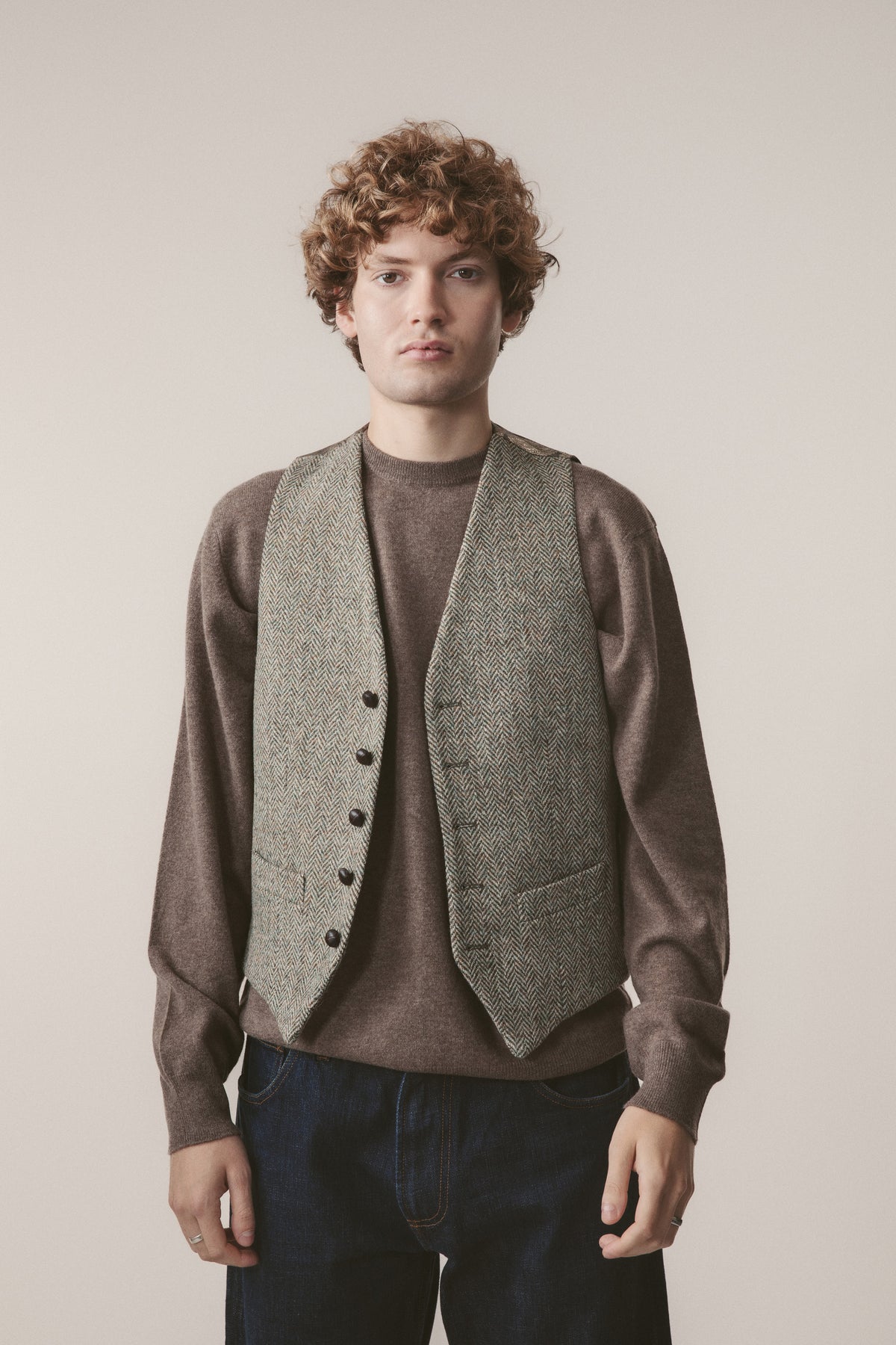 Harris Tweed Iain Waistcoat in Green Lovat Herringbone worn open over a brown crewneck sweater, front view on model