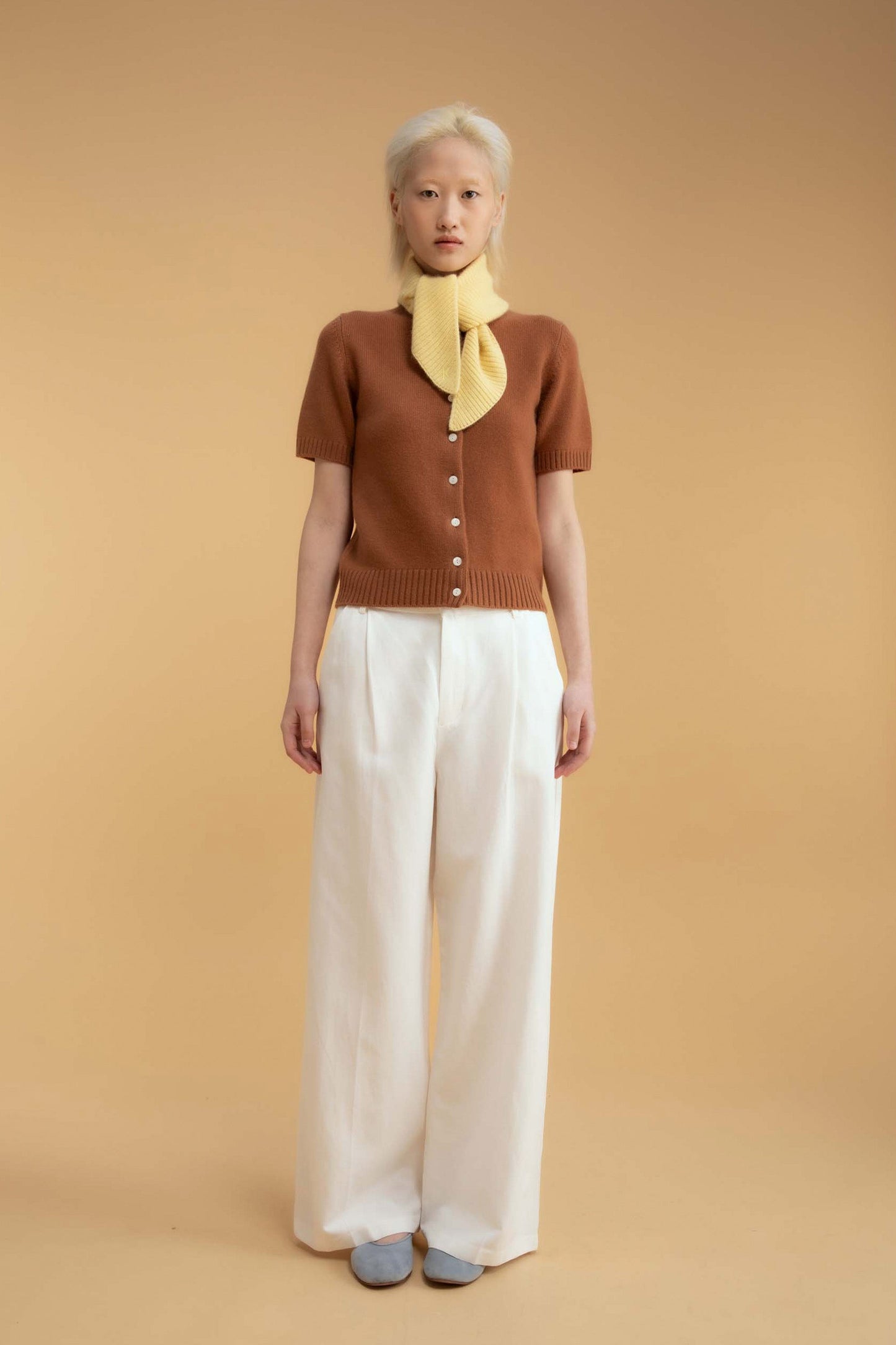 Knitted Cashmere Neck Tie in Lemon Sherbet styled knotted at the neck over a brown short-sleeve cardigan and white trousers