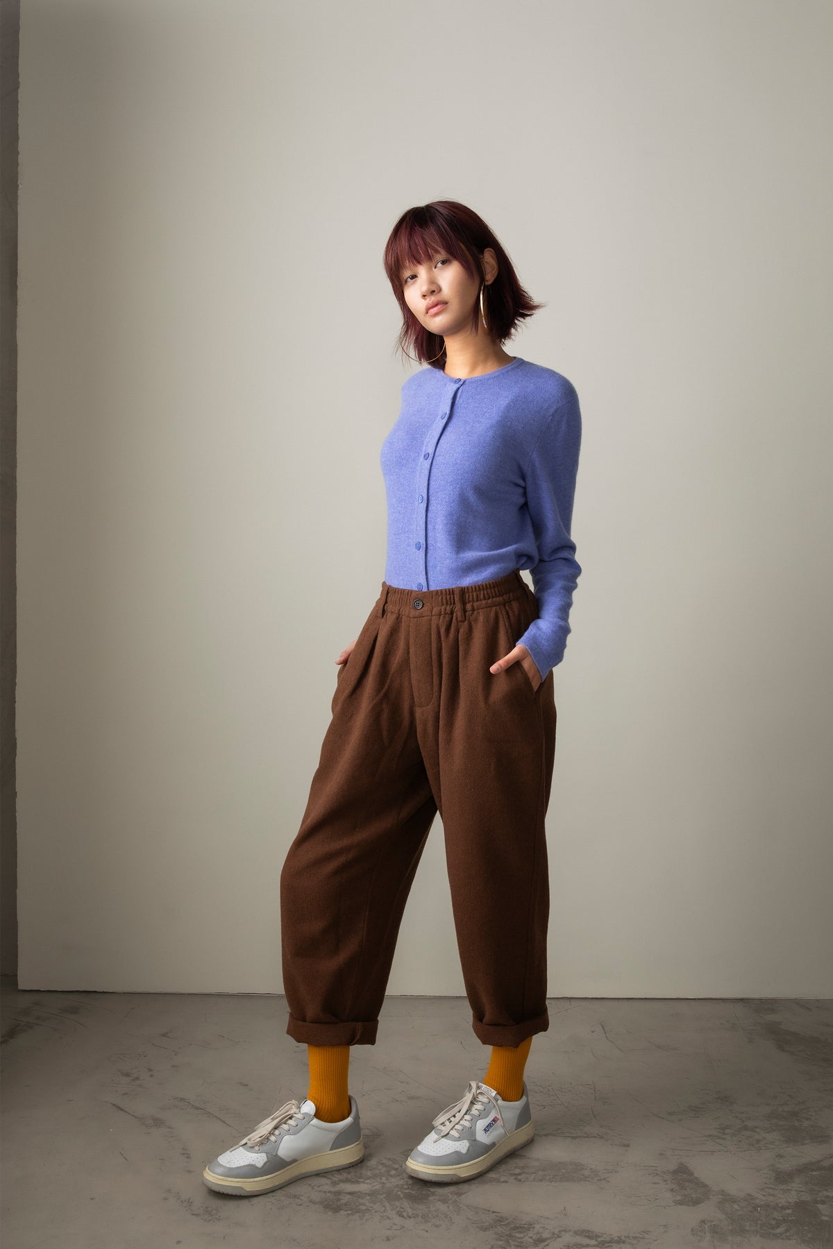 Model wearing Wisteria Women's Cashmere High Button Cardigan in periwinkle blue, styled tucked into brown trousers, full-length view
