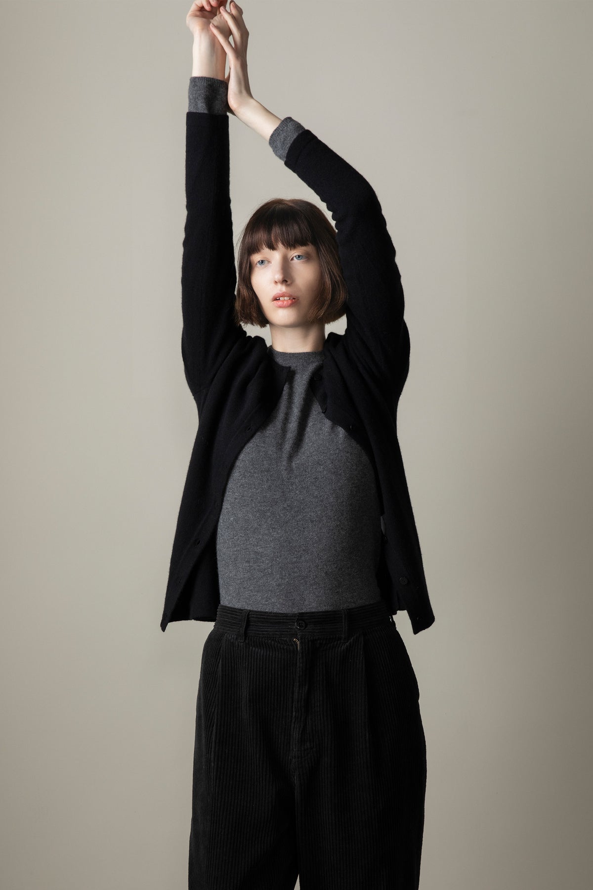 Women's Cashmere High Button Cardigan in black worn open over a grey crew neck top, arms raised to show relaxed fit