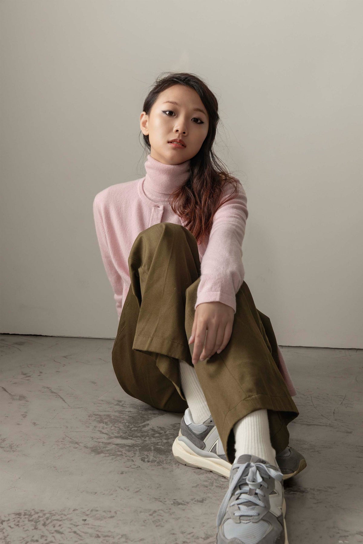 Model seated on floor wearing Women's Cashmere High Button Cardigan in Pale Lilac over a matching turtleneck, styled with olive trousers